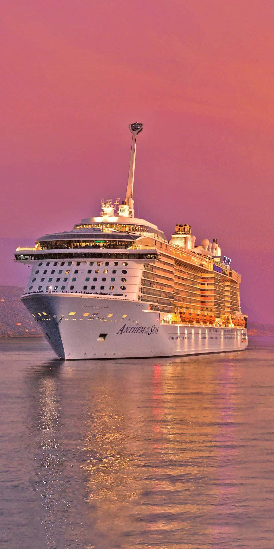 Cruise 桌布 壁紙 — 郵輪 Anthem of the Seas 在充滿活力的粉紅色暮色天空中溫暖地發光，其燈光在平靜的水面上反射。