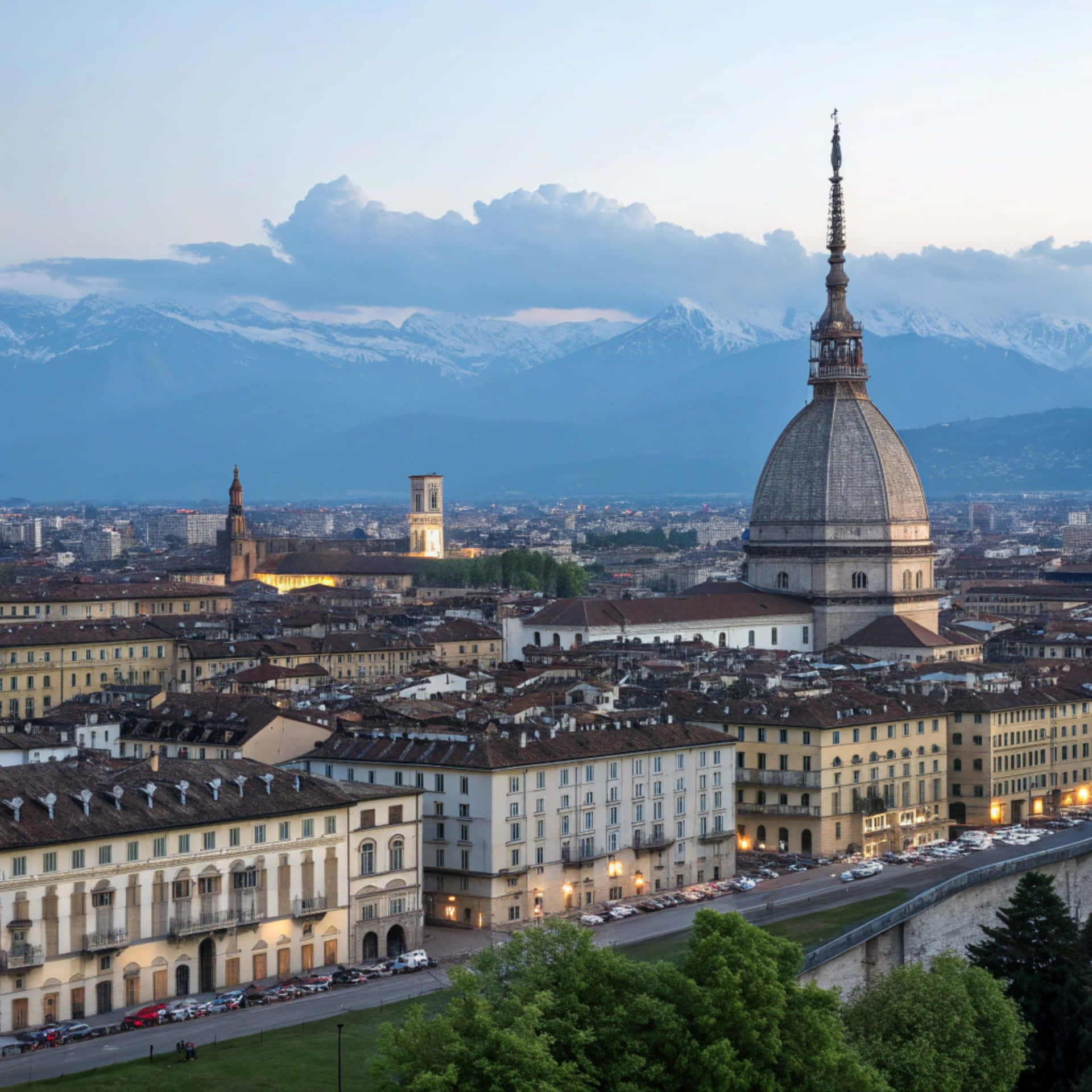 Skyline Turin 壁紙 — 都靈黃昏時分的全景，安東內利尖塔聳立在歷史建築和遠處積雪的山峰之上。