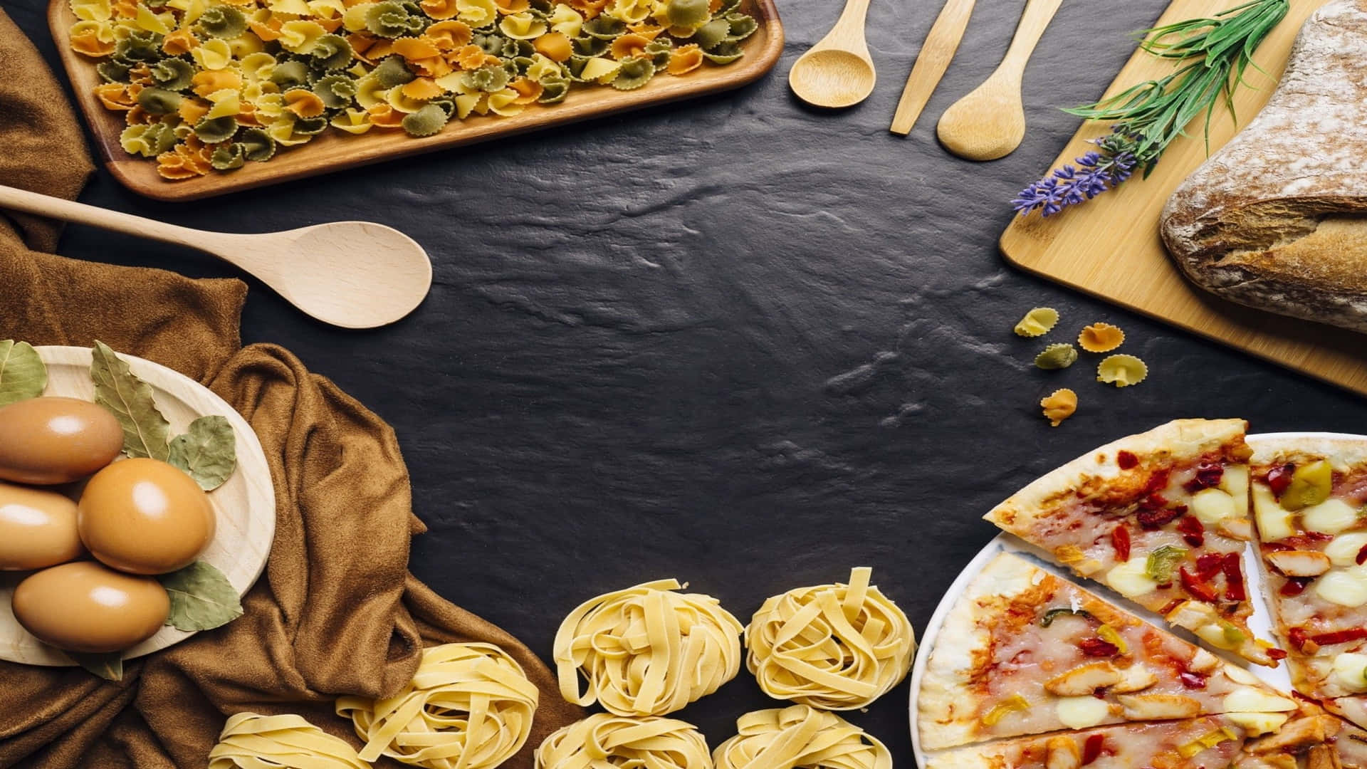 Italian 桌布 壁紙 — 鄉村風味食物拼盤，包括色彩繽紛的義大利麵、雞蛋、麵包和披薩，擺放在深色石板表面上，配以木製餐具和香草。