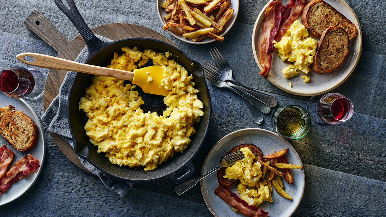 Scrambled Egg 桌布 壁紙 — 鄉村風早餐，有鬆軟炒蛋、培根和香脆薯條，盛在盤中，上方掛著一個鑄鐵鍋。