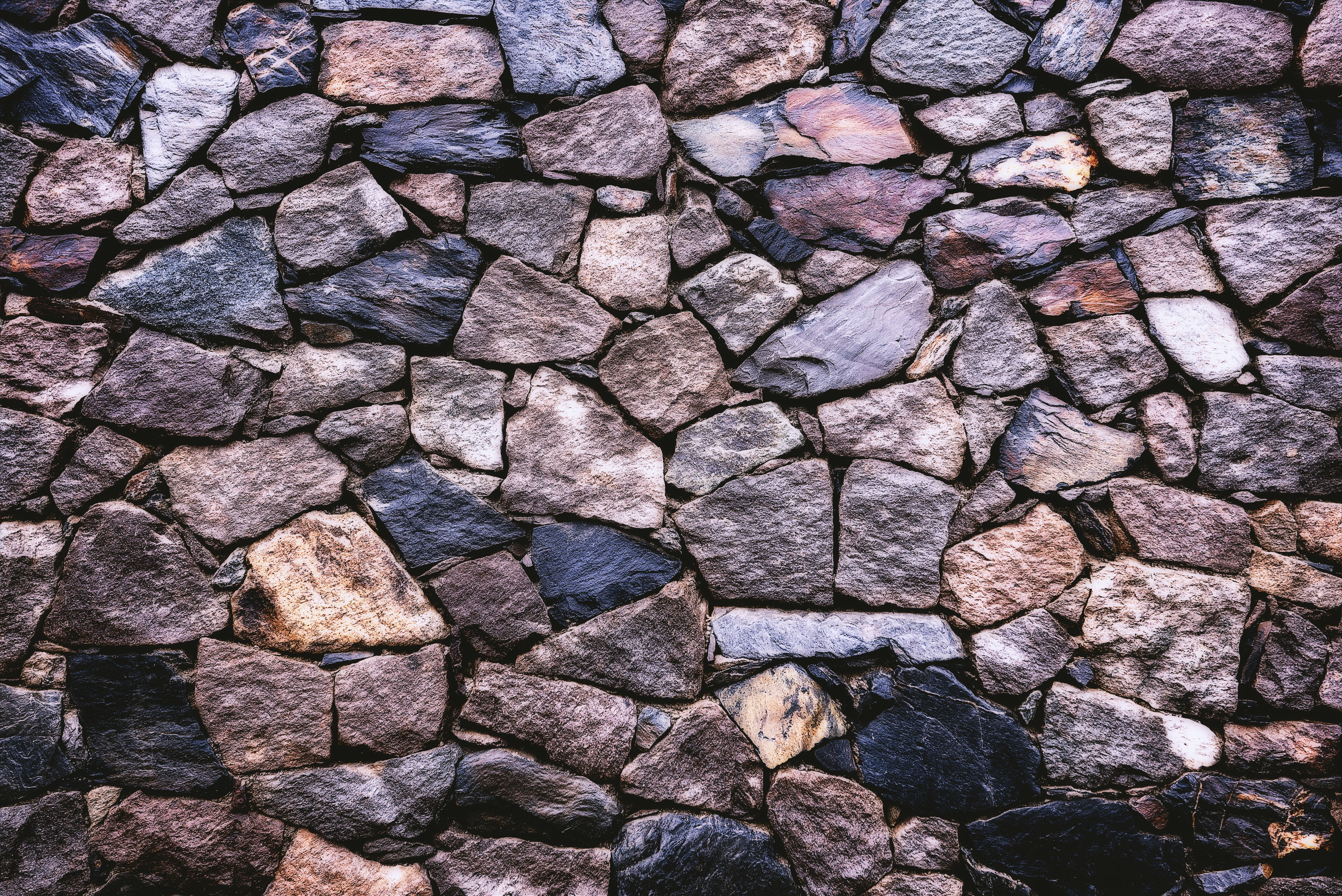 Stone 桌布 壁紙 — 鄉村風格石牆的近距離特寫，呈現多種大地色調和粗糙質感。