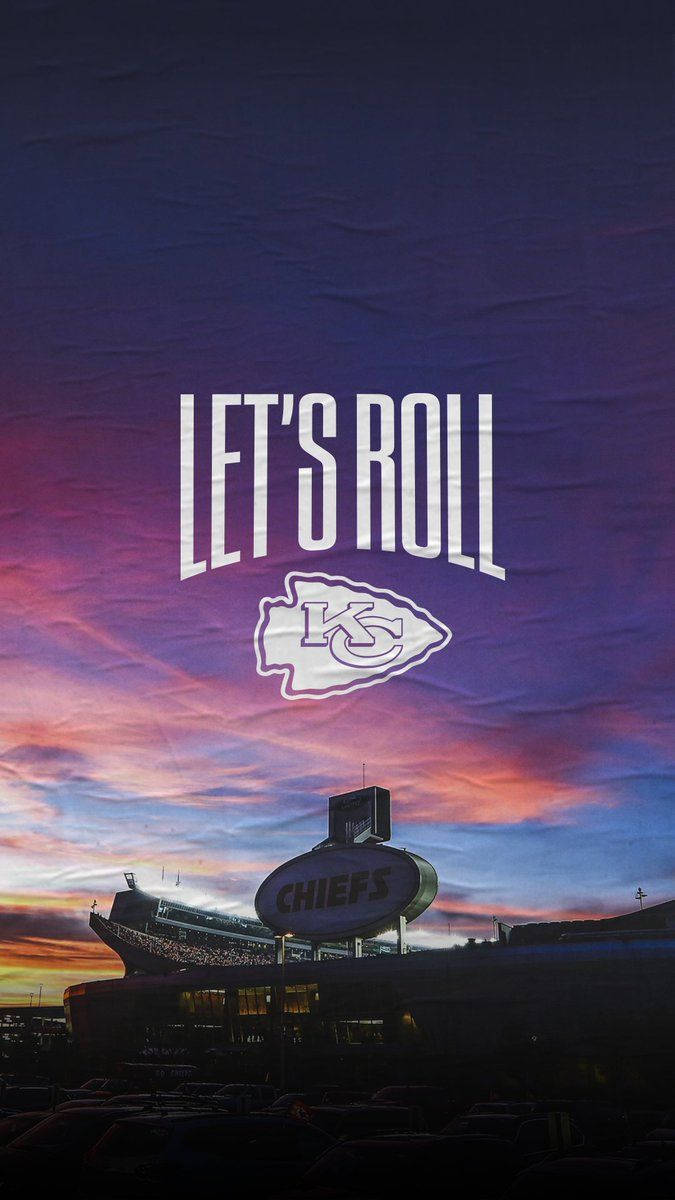Kc Chiefs 桌布 壁紙 — 酋長隊球場在日落時分，帶有「LET'S ROLL」文字和標誌，襯托著充滿活力的紫橙色天空。
