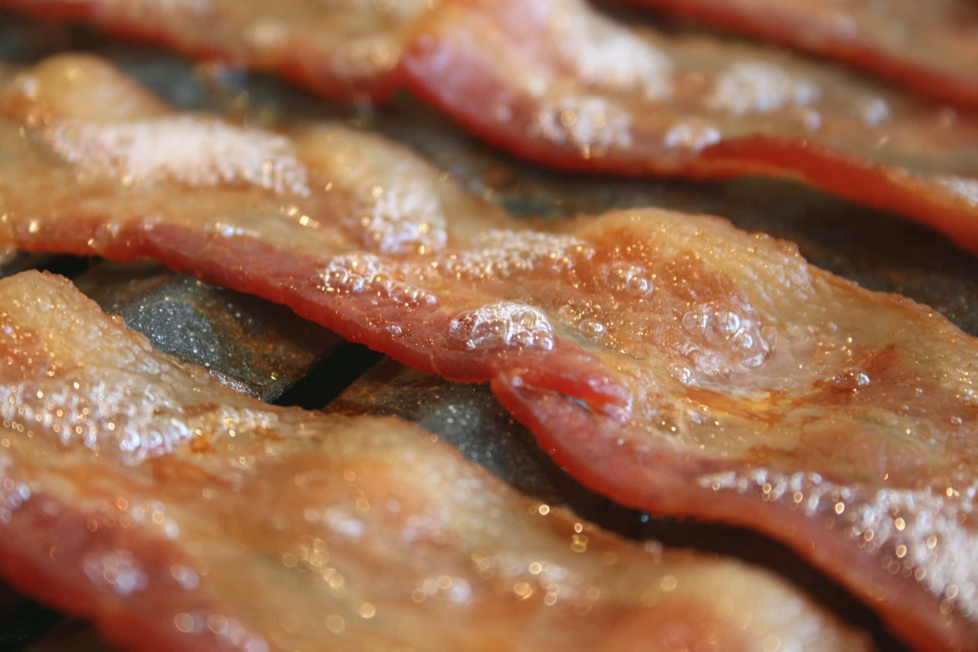 bacon 桌布 壁紙 — 酥脆的培根條在黑色烤盤上滋滋作響，金黃的油脂冒泡。