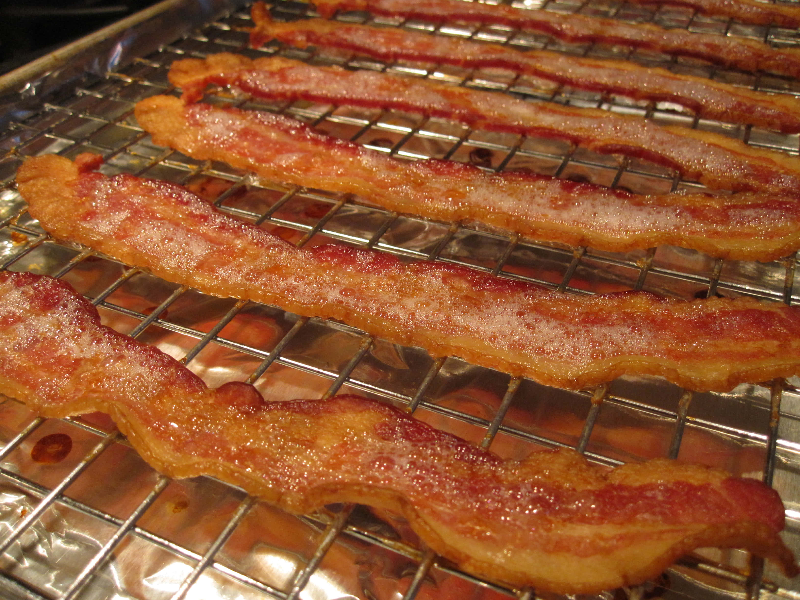 bacon 桌布 壁紙 — 酥脆金黃的培根條在金屬冷卻架上閃爍著油脂，下方墊有錫箔紙。