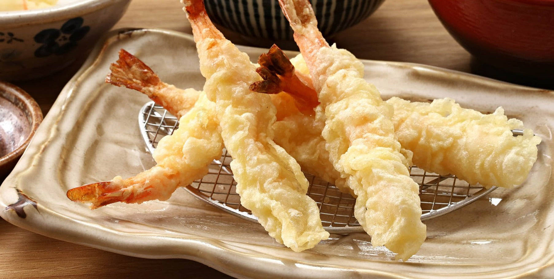 shrimp 桌布 壁紙 — 酥脆金黃的天婦羅蝦放在陶瓷盤上的金屬架上，背景是柔焦的傳統日本碗。