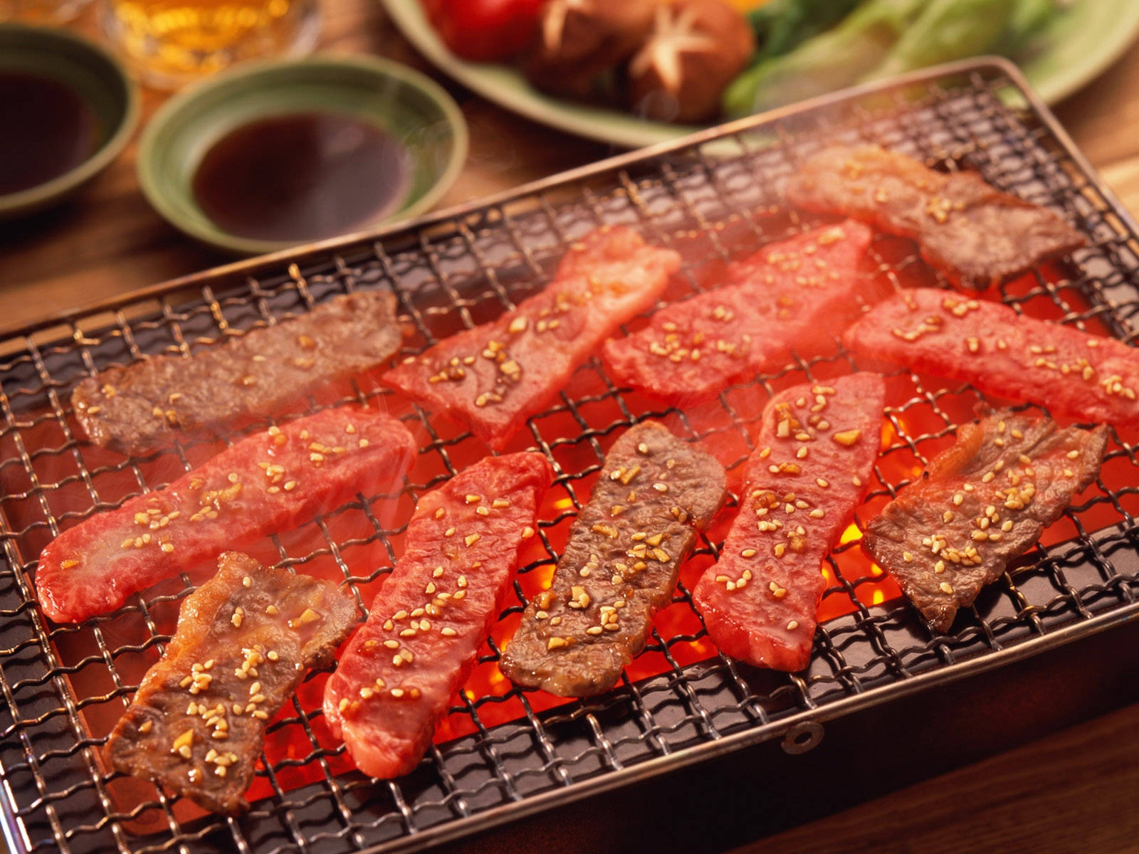 meat 桌布 壁紙 — 醃製牛肉條和生肉在熾熱炭火上的金屬烤架上烤得滋滋作響，配上芝麻和配菜。