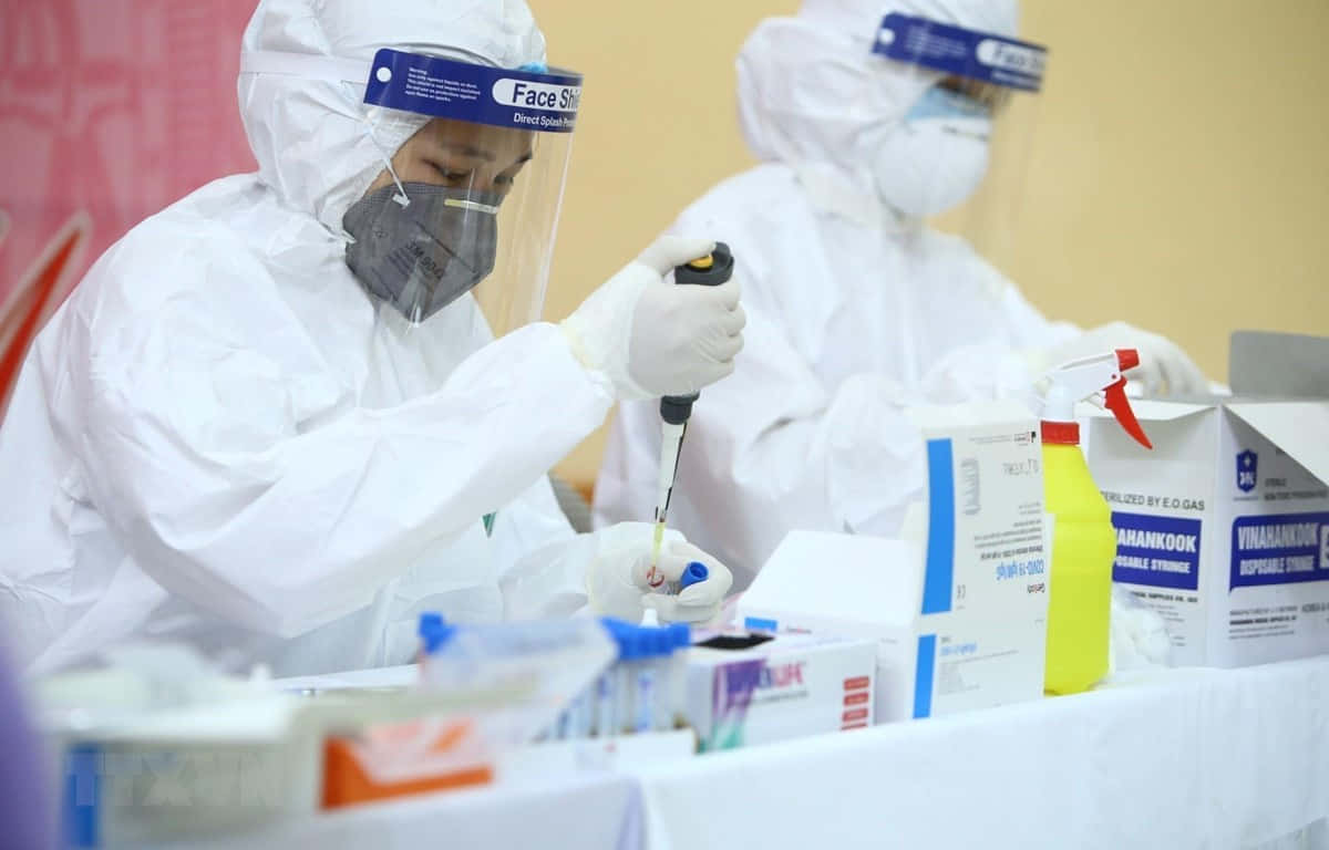 醫生 桌布 壁紙 — 醫護人員穿著全套防護裝備，在健康篩查操作期間於實驗室站小心處理試管。