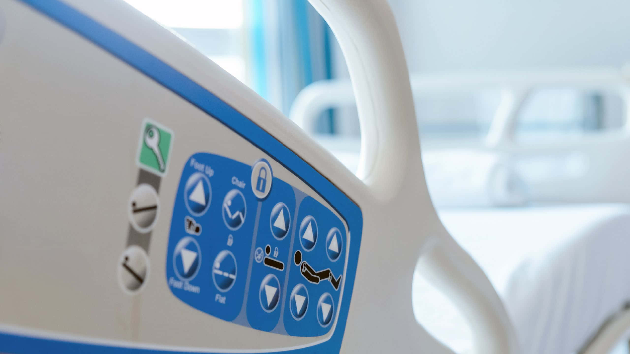 Hospital Bed 桌布 壁紙 — 醫院病床控制面板的特寫，帶有藍色按鈕和用於調整病人位置的圖標。