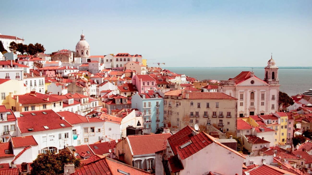 Portugal 桌布 壁紙 — 里斯本歷史區的陽光全景，赤陶屋頂和柔和色調的建築俯瞰海洋。