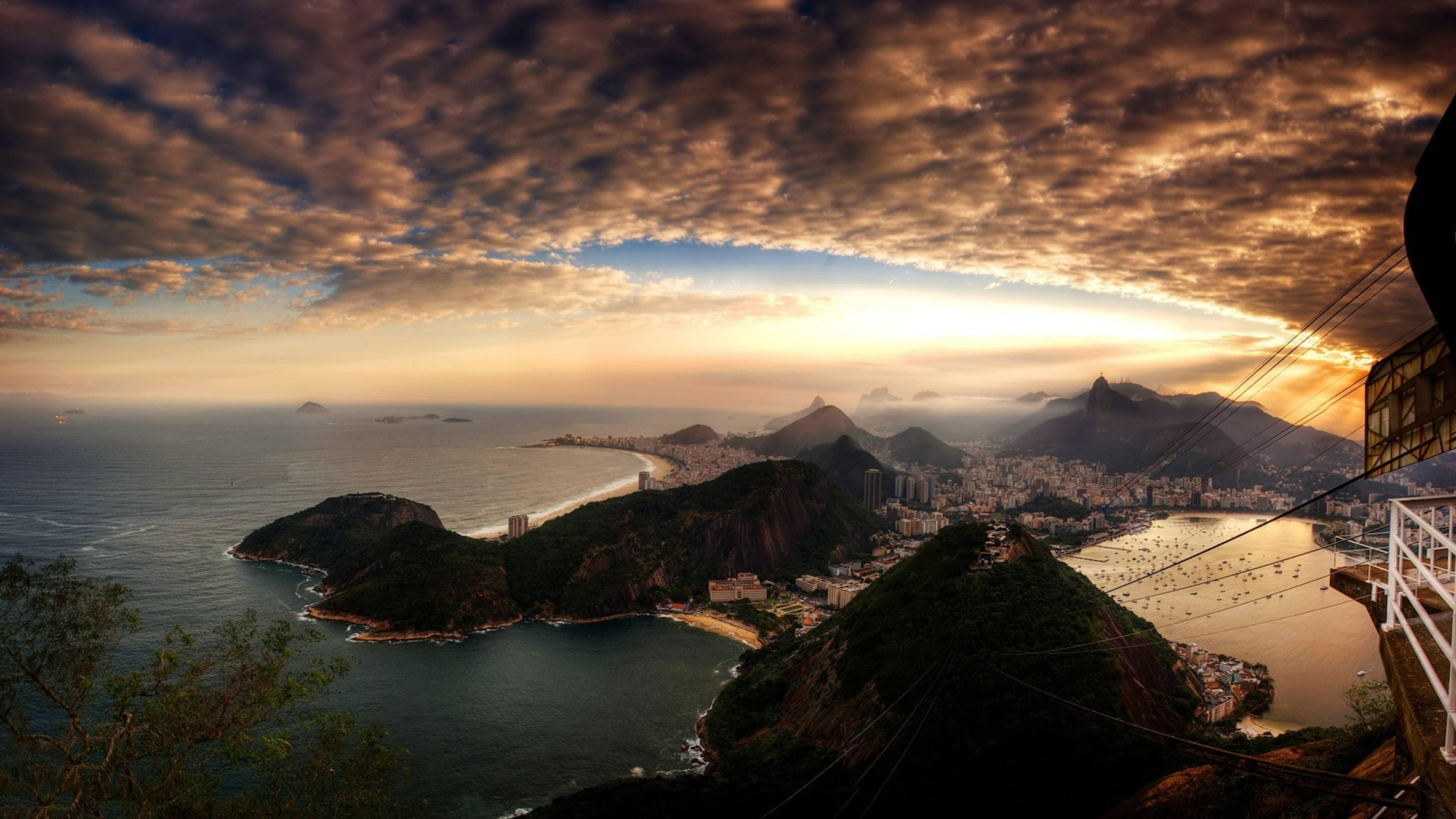 rio 桌布 壁紙 — 里約熱內盧令人驚嘆的日落，金色雲朵將溫暖的光芒灑向城市和下方的海洋。