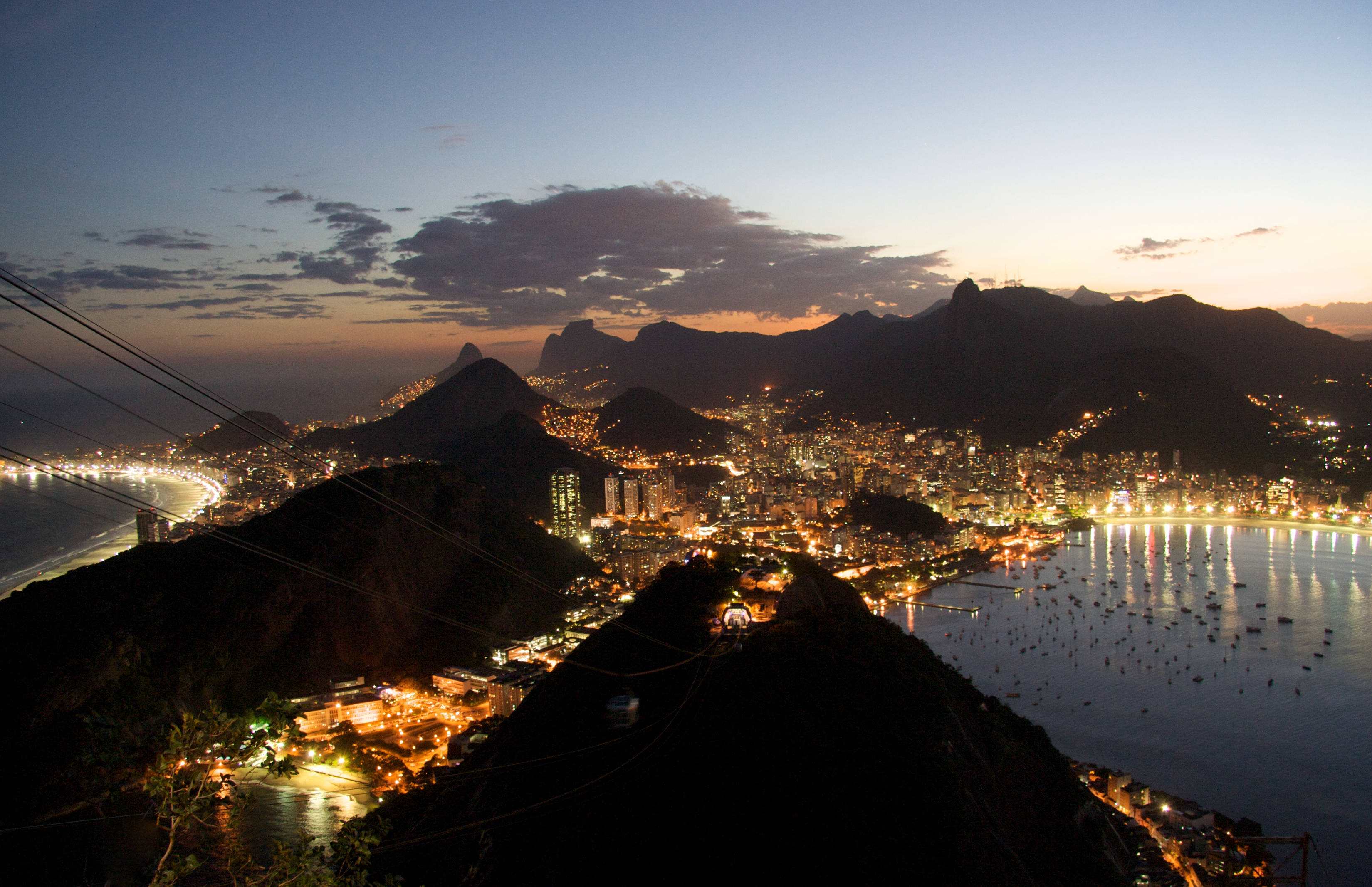 South America 桌布 壁紙 — 里約熱內盧在暮色中閃耀的城市景觀，坐落於山脈與閃爍海灣之間，令人嘆為觀止。