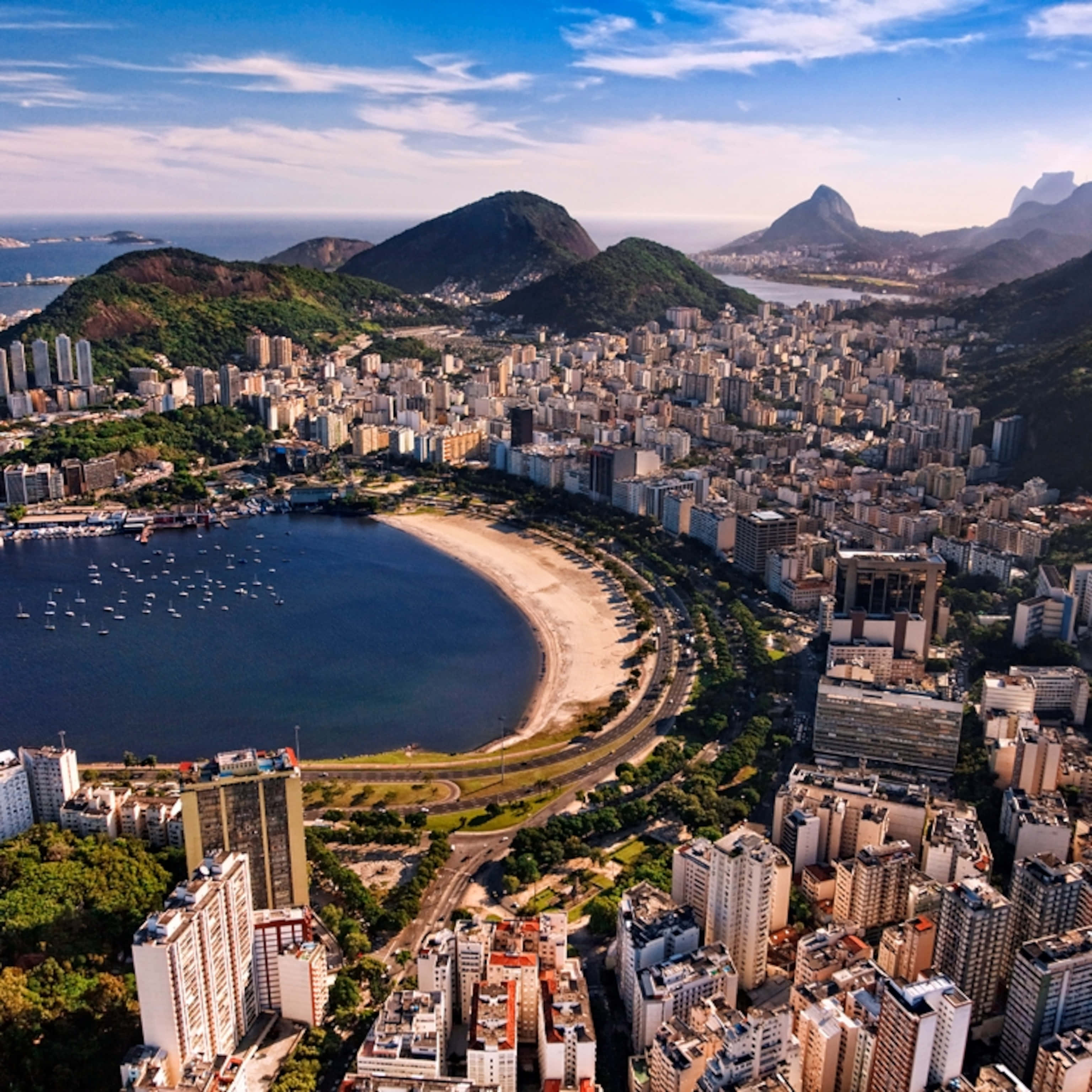 Brazilian Beach 桌布 壁紙 — 里約熱內盧標誌性海岸線的鳥瞰圖，包括糖麵包山和科帕卡巴納海灘，周圍是密集的城市建築，天空湛藍。