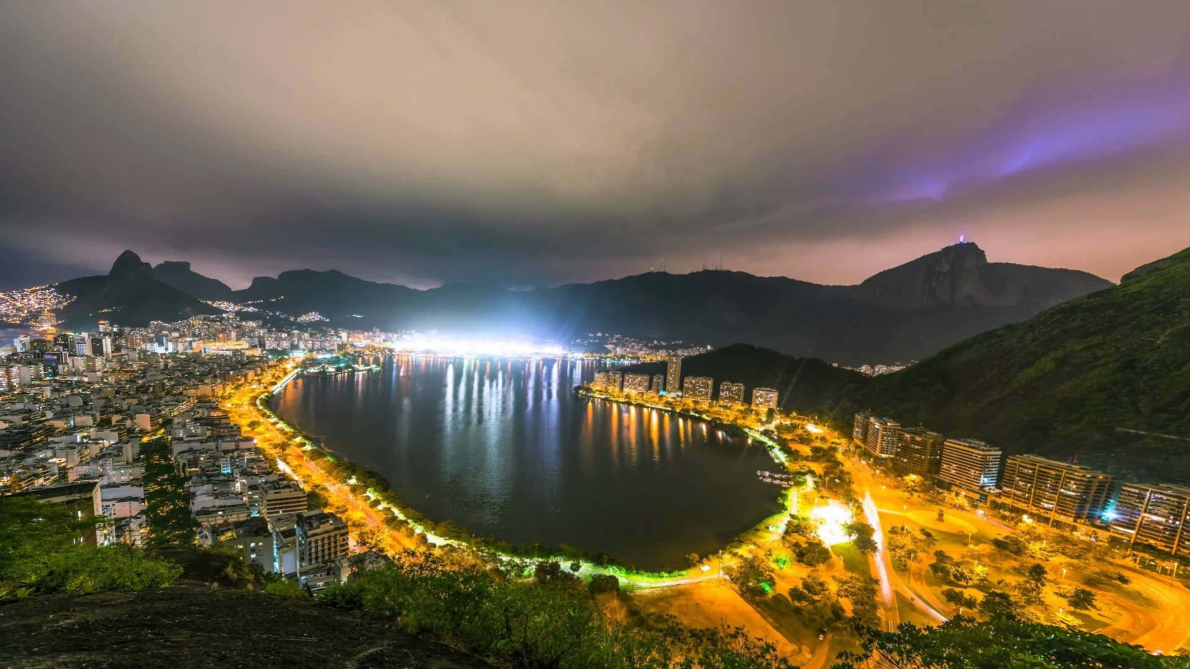 極高畫質 桌布 壁紙 — 里約熱內盧海岸線充滿活力的夜景，城市燈光在水面上閃爍，背景是山脈。