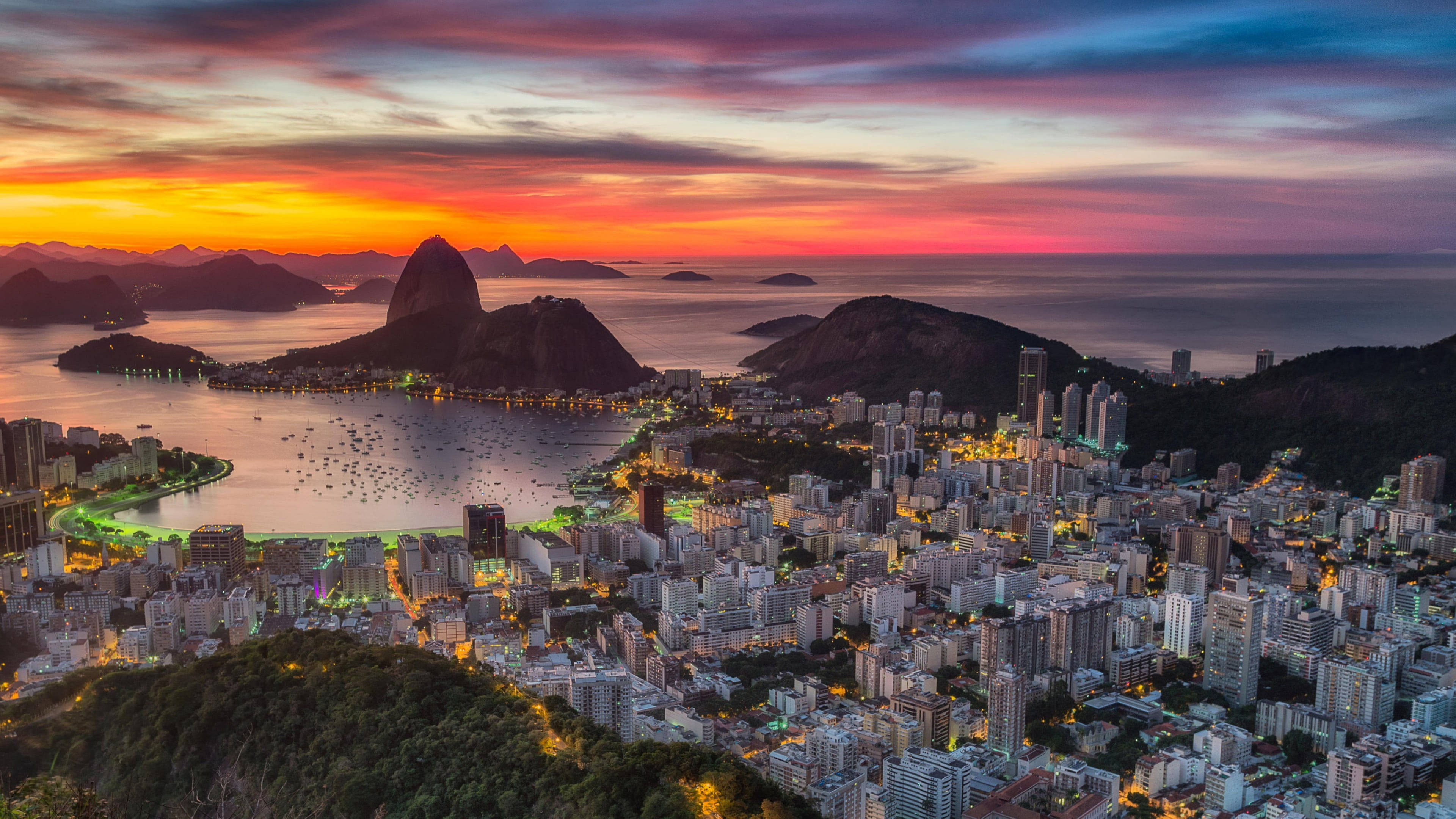 rio 桌布 壁紙 — 里約熱內盧的鳥瞰圖，日落時分，甜麵包山和城市燈光在火紅的橙色和紫色天空下閃耀。