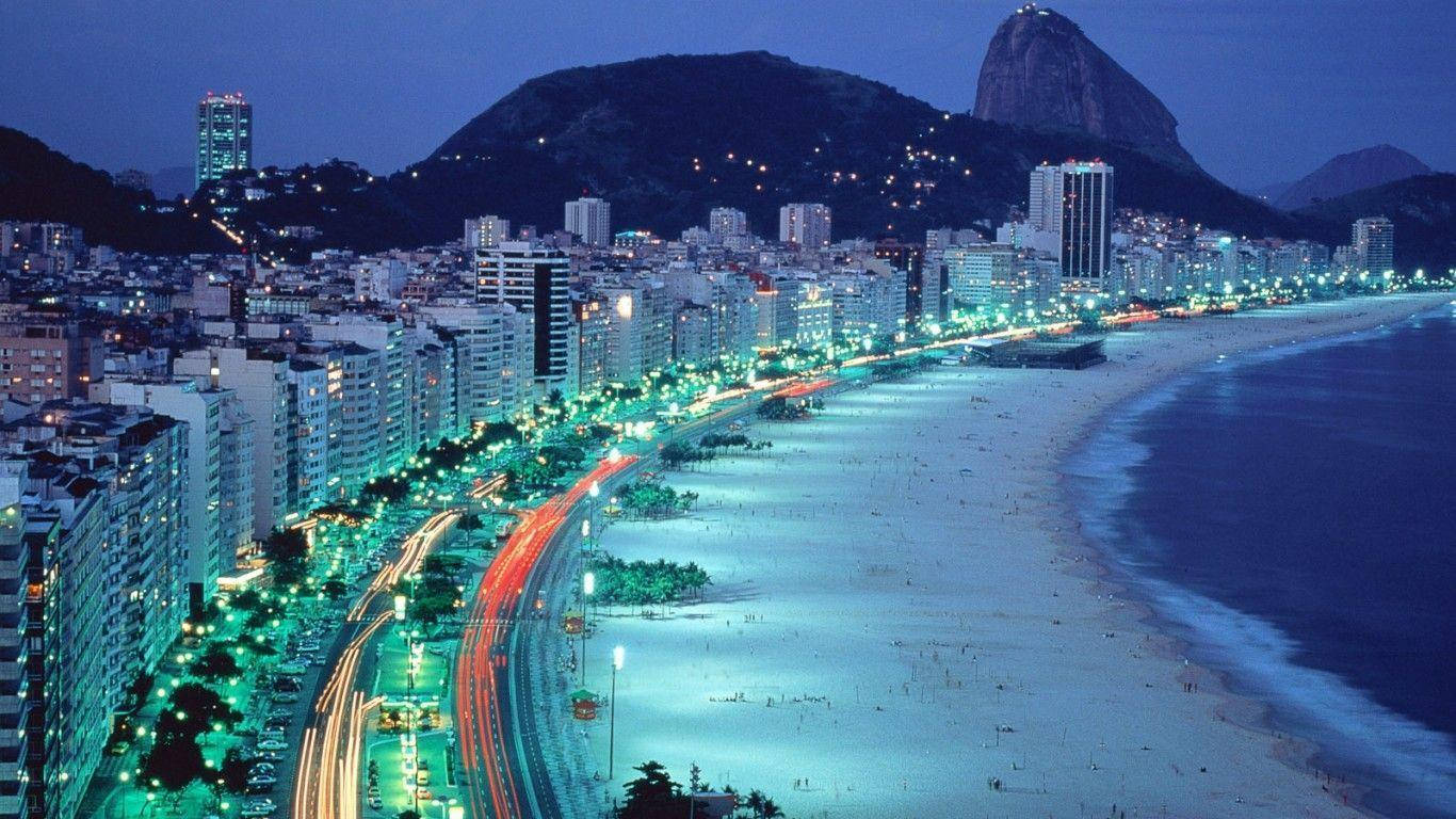 South America 桌布 壁紙 — 里約熱內盧科帕卡巴納海灘的充滿活力的夜景，城市燈光閃爍，背景是標誌性的甜麵包山。