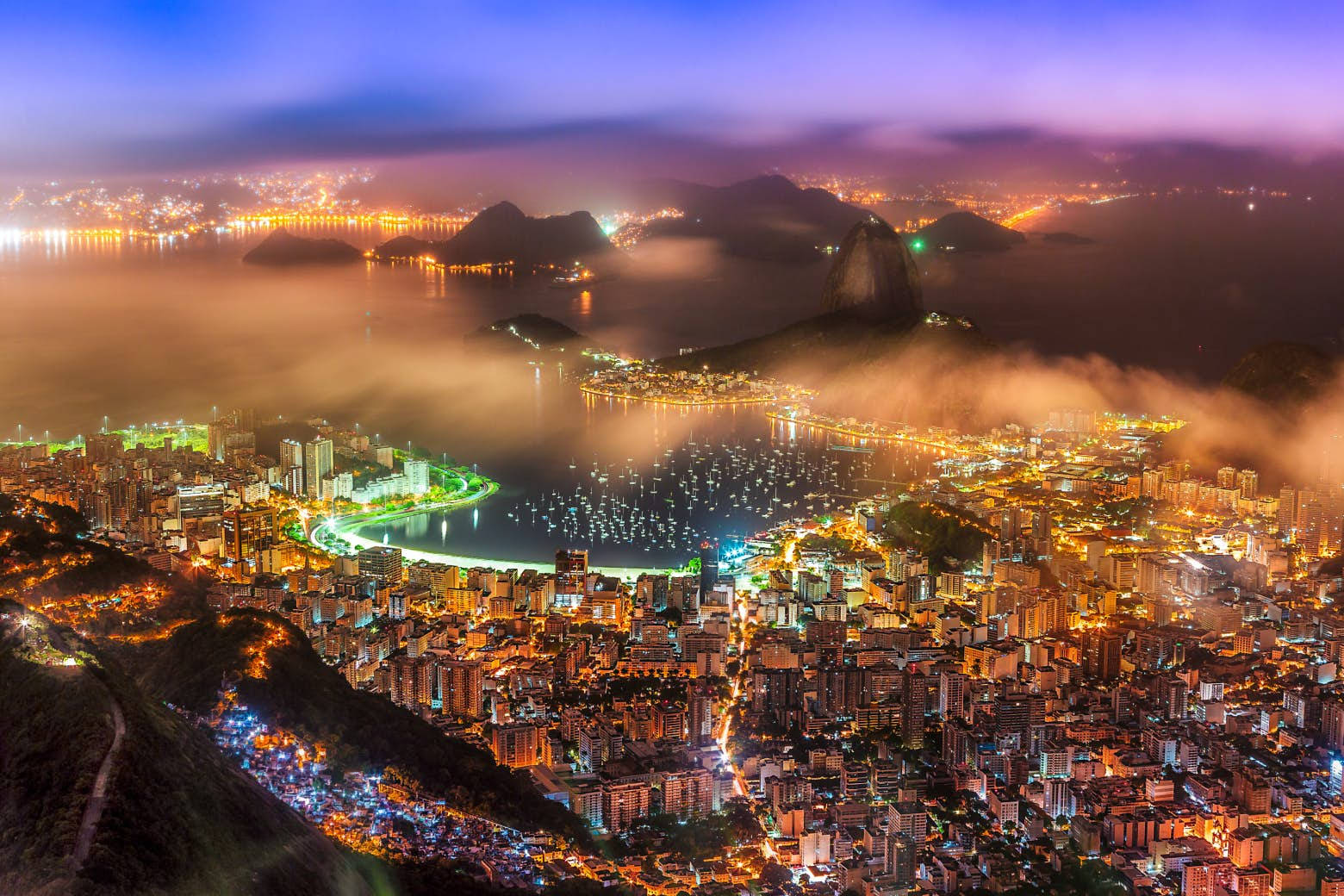 South America 桌布 壁紙 — 里約熱內盧黃昏時的鳥瞰圖，城市燈光在霧氣繚繞的山巒和充滿活力的海灣中閃爍。