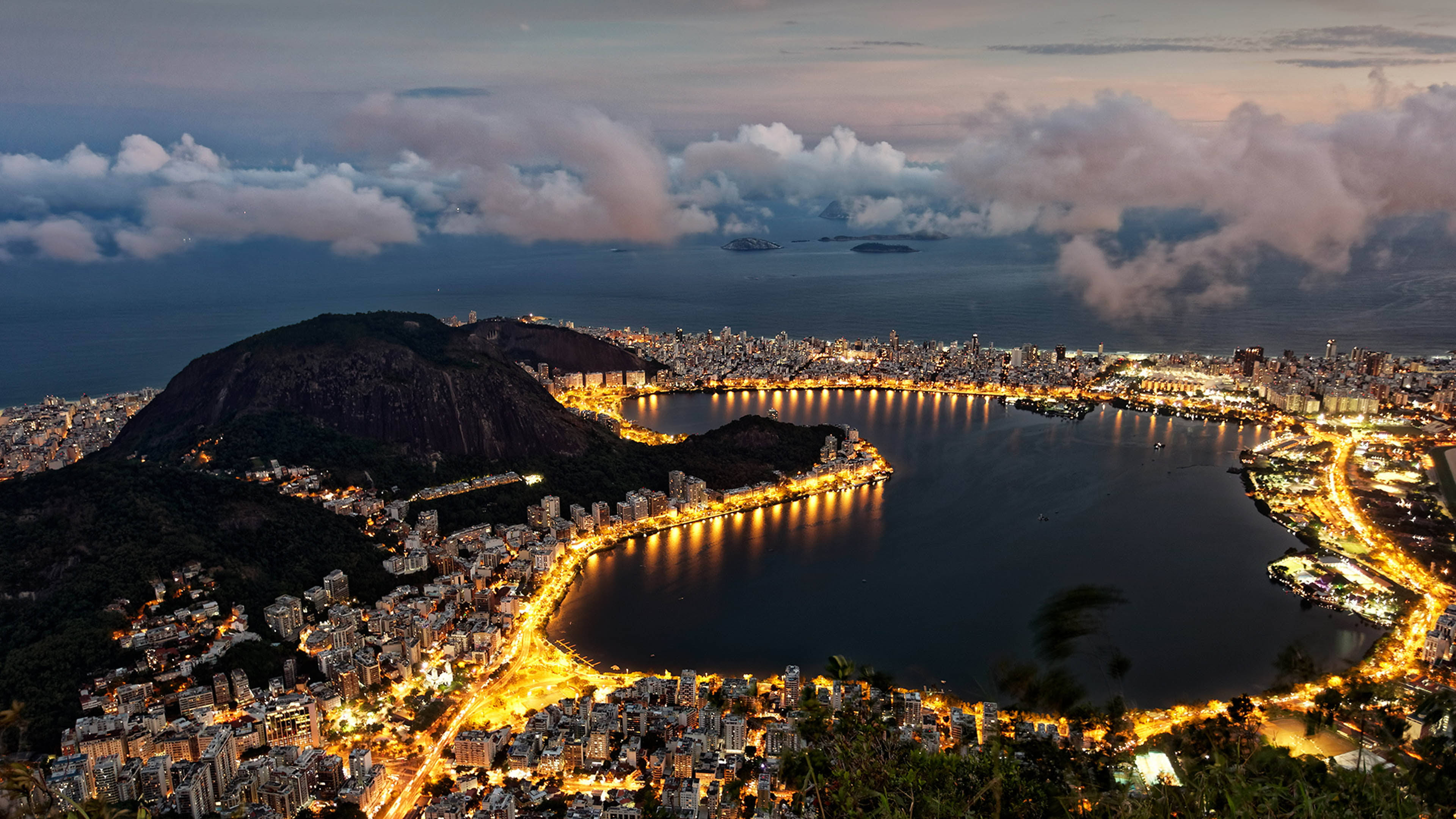 rio 桌布 壁紙 — 里約熱內盧黃昏時的鳥瞰圖，糖麵包山和閃爍的城市燈光擁抱著海灣。