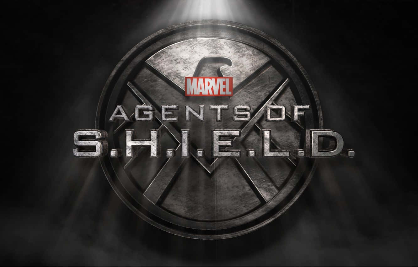 Marvel Logo 桌布 壁紙 — 金屬S.H.I.E.L.D.標誌在聚光燈下發光，背景黑暗煙霧繚繞，上方有Marvel標誌。