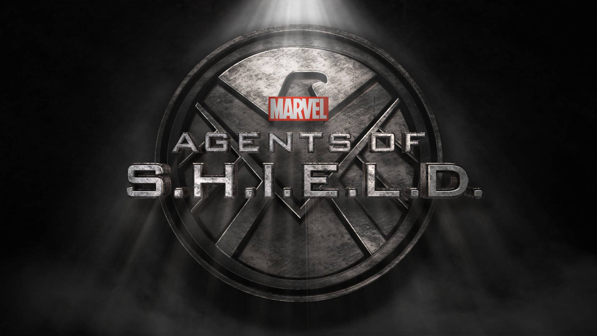 漫威 桌布 壁紙 — 金屬S.H.I.E.L.D.標誌在聚光燈下發光，背景是煙霧瀰漫的黑暗，上方有Marvel標誌。