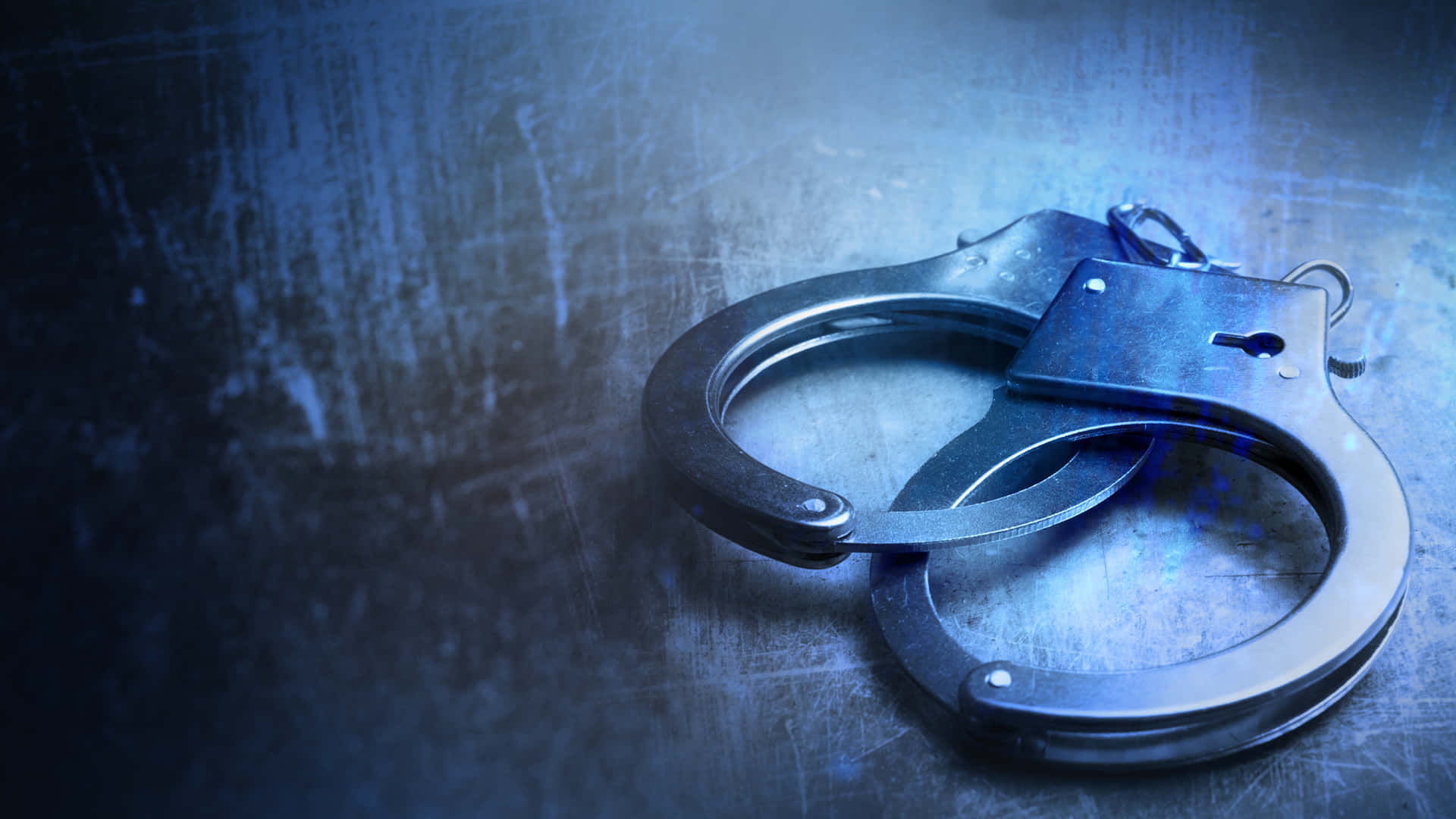 Law Enforcement 桌布 壁紙 — 金屬手銬在戲劇性燈光下放置於有刮痕的藍色表面上。