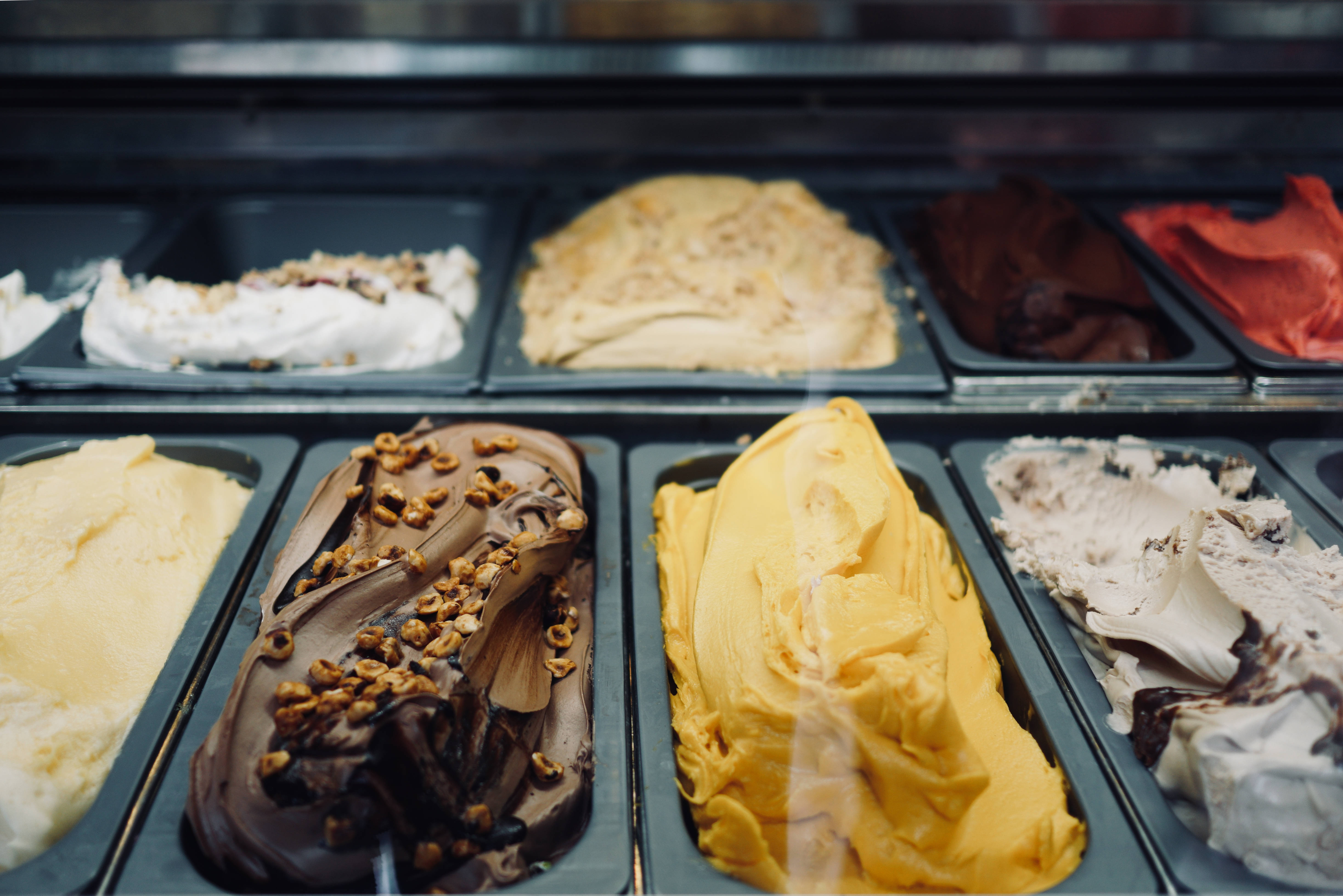 Ice Cream 桌布 壁紙 — 金屬桶中一排排色彩繽紛的義式冰淇淋，在柔和溫暖的燈光下展現出巧克力、焦糖、香草和草莓的奶油漩渦。
