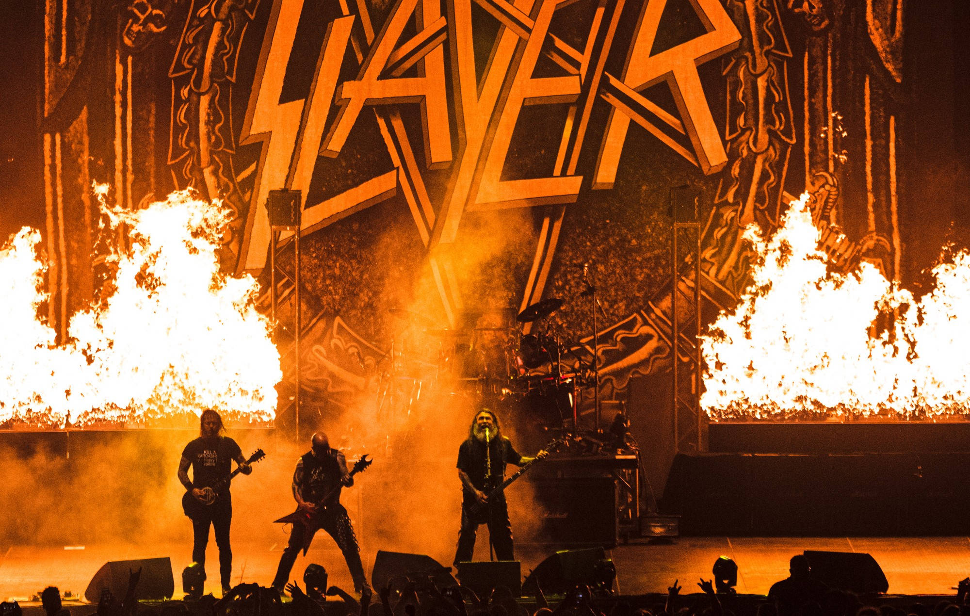 Slayer 桌布 壁紙 — 金屬樂隊 Slayer 在熾熱的舞台上表演，兩側火焰在強烈的橙色燈光下噴發。