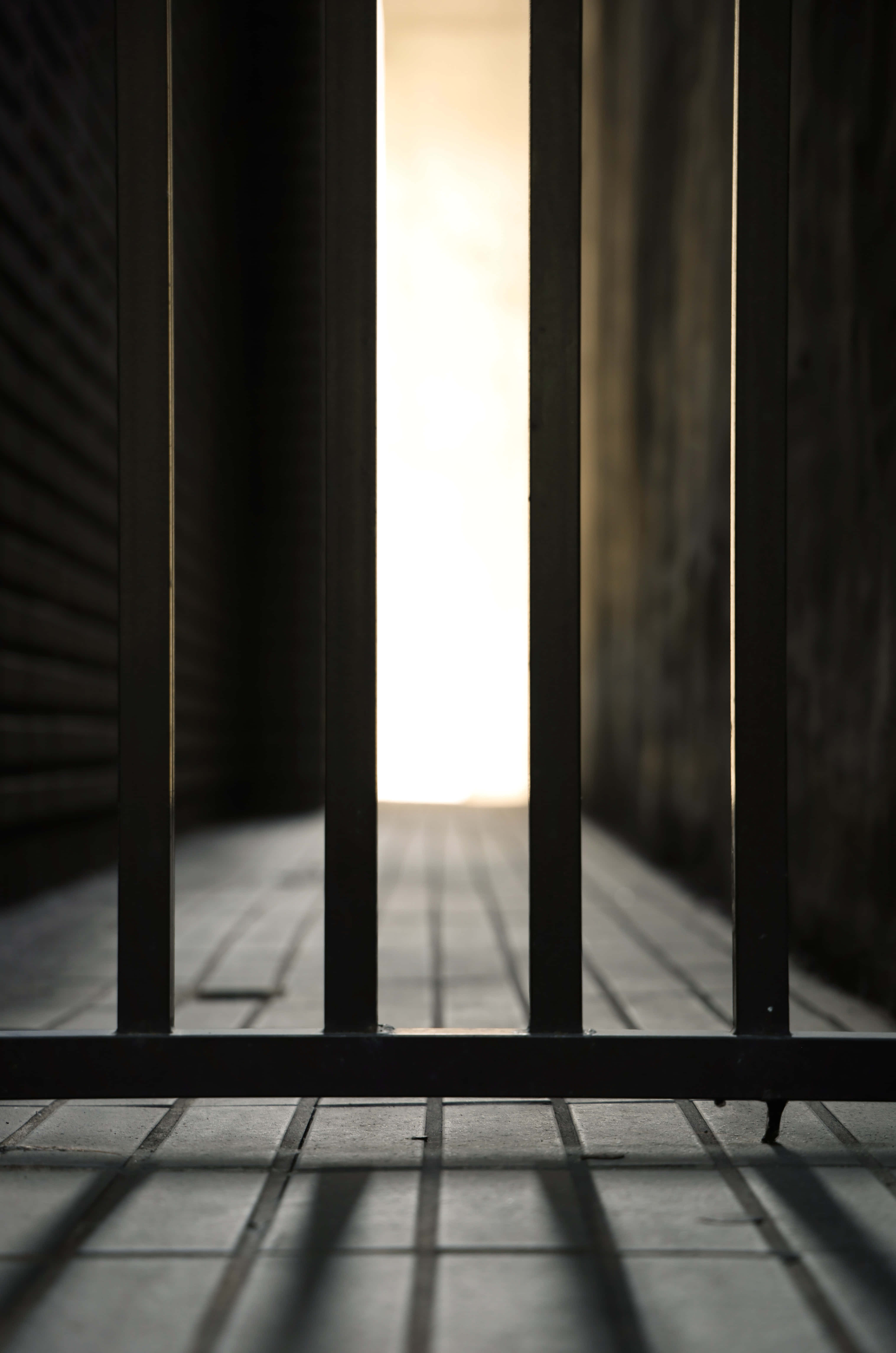 Prison 桌布 壁紙 — 金屬欄杆後一條狹窄的走廊，沐浴在遠處開口透進的溫暖光線中。