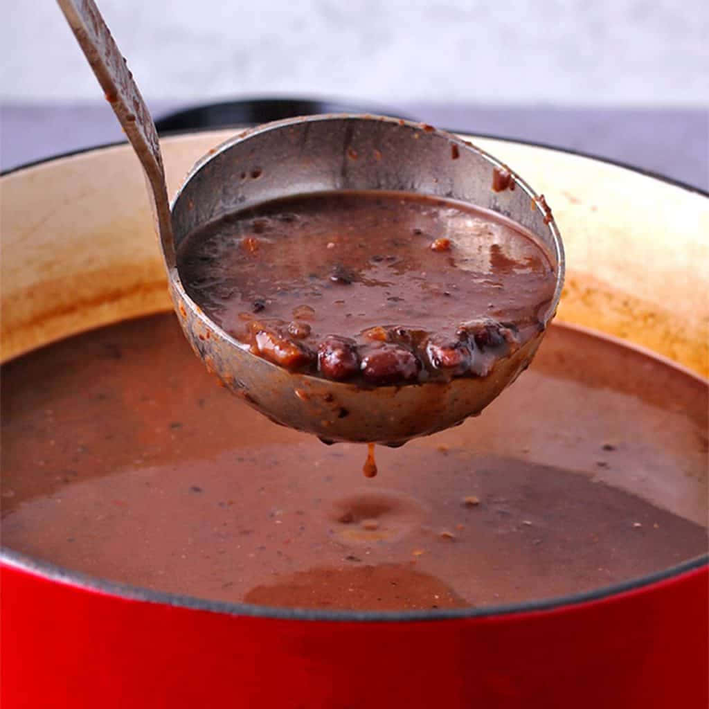 Black Bean Soup 桌布 壁紙 — 金屬湯勺從鮮紅色的琺瑯鑄鐵鍋中舀起濃稠的深紅色豆燉肉。