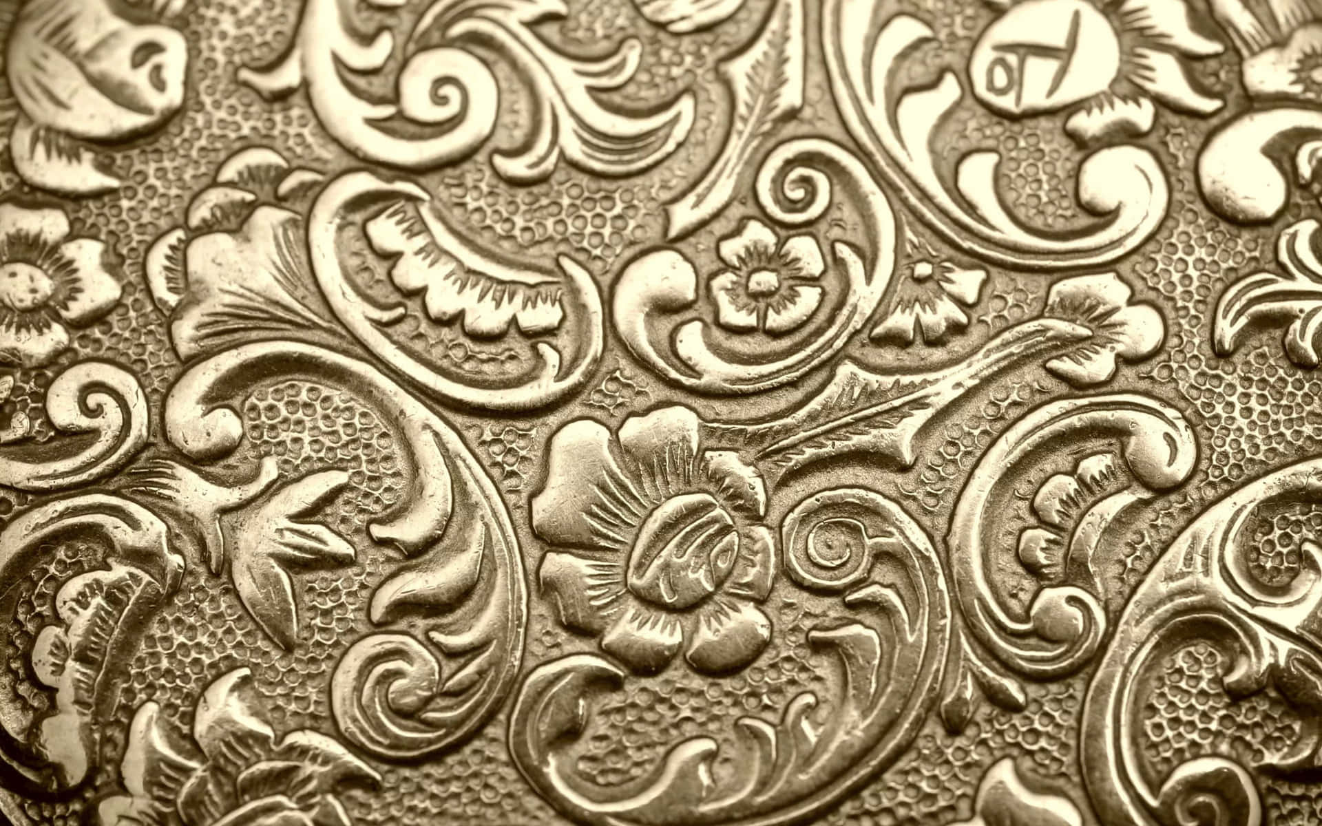 圖案 桌布 壁紙 — 金屬紋理表面上複雜的金色壓花花卉和捲軸圖案的近距離特寫。