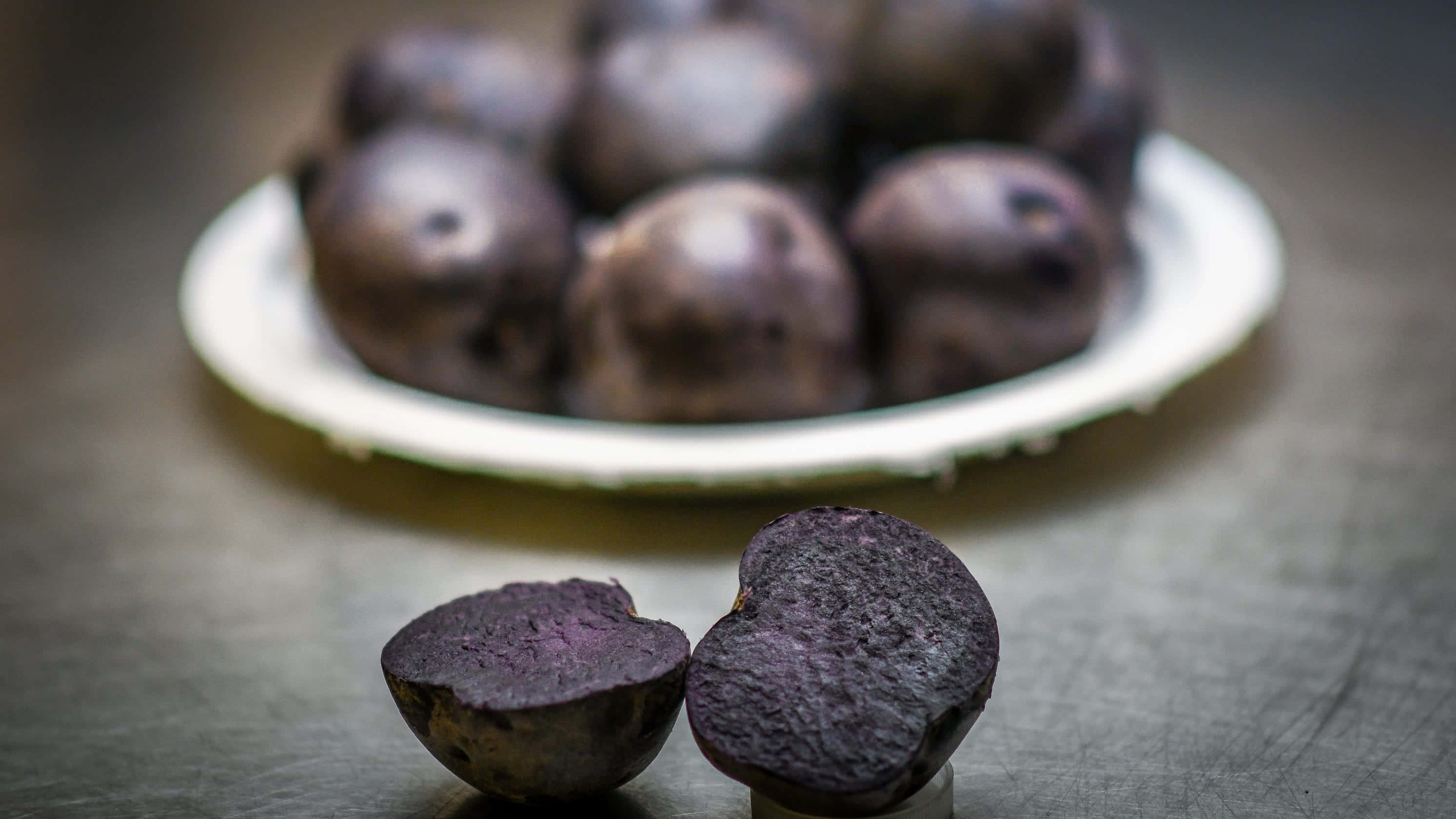 Purple Potato 桌布 壁紙 — 金屬表面上的紫色甜菜切半特寫，後面有模糊的整顆甜菜盤。