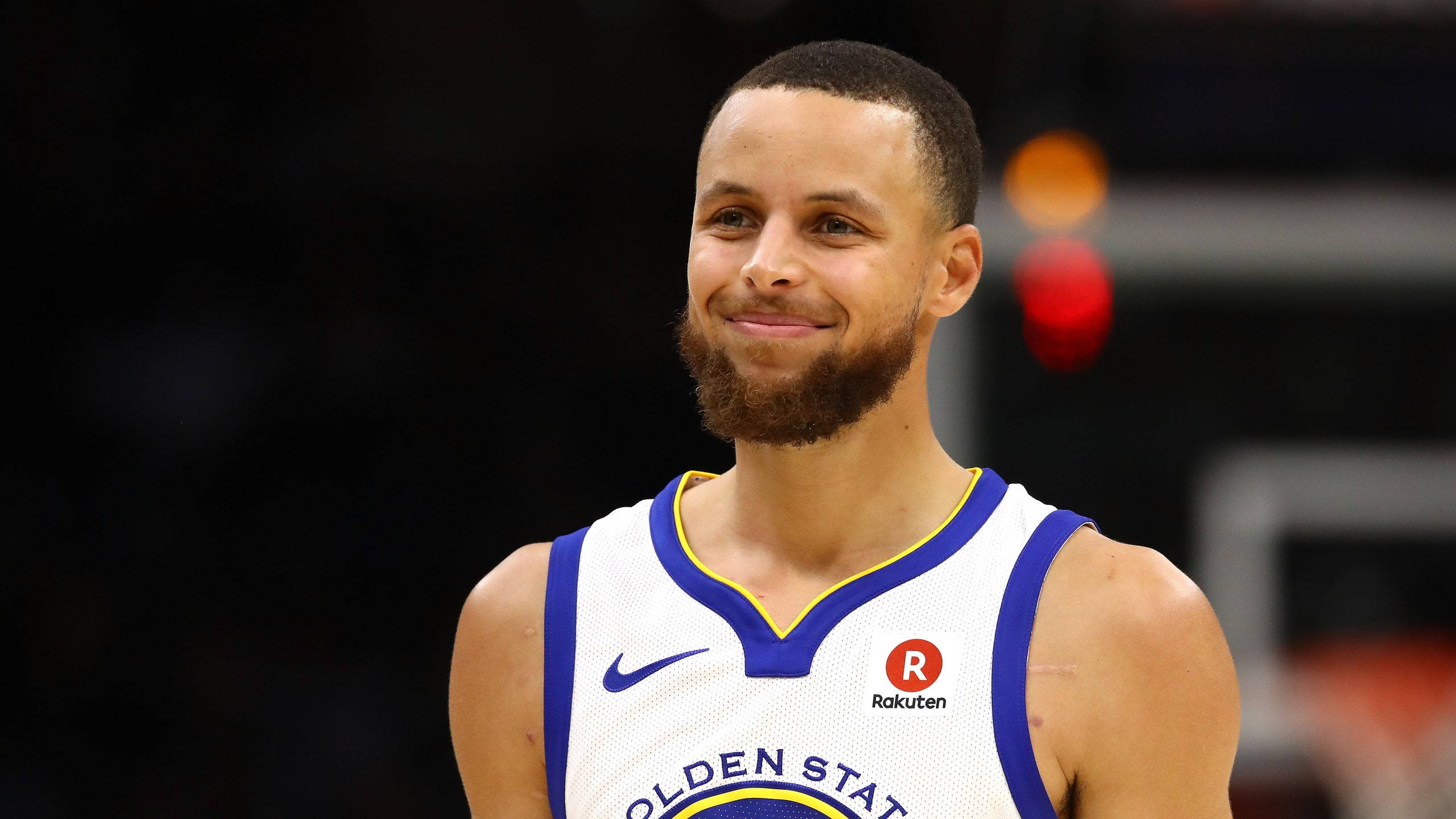 NBA 桌布 壁紙 — 金州勇士籃球運動員史蒂芬柯瑞在比賽中穿著白色和藍色球衣自信地微笑。