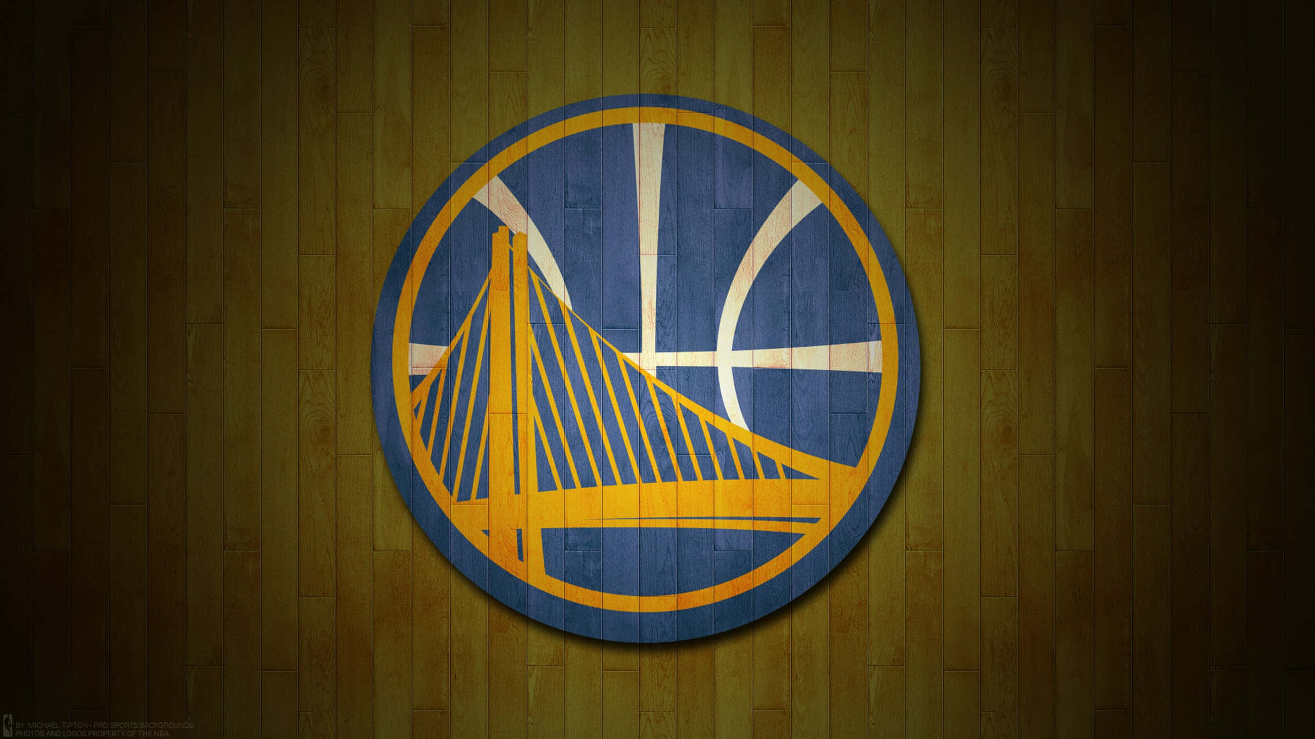 Golden State Warriors Logo 桌布 壁紙 — 金州勇士隊標誌繪於木製籃球場牆上，配以溫暖的環境燈光。
