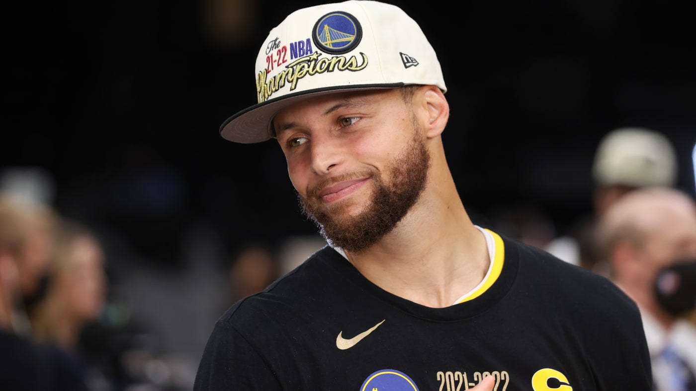 籃球 桌布 壁紙 — 金州勇士隊球星史蒂芬柯瑞戴著2021-2022年NBA冠軍帽和球隊衫微笑。