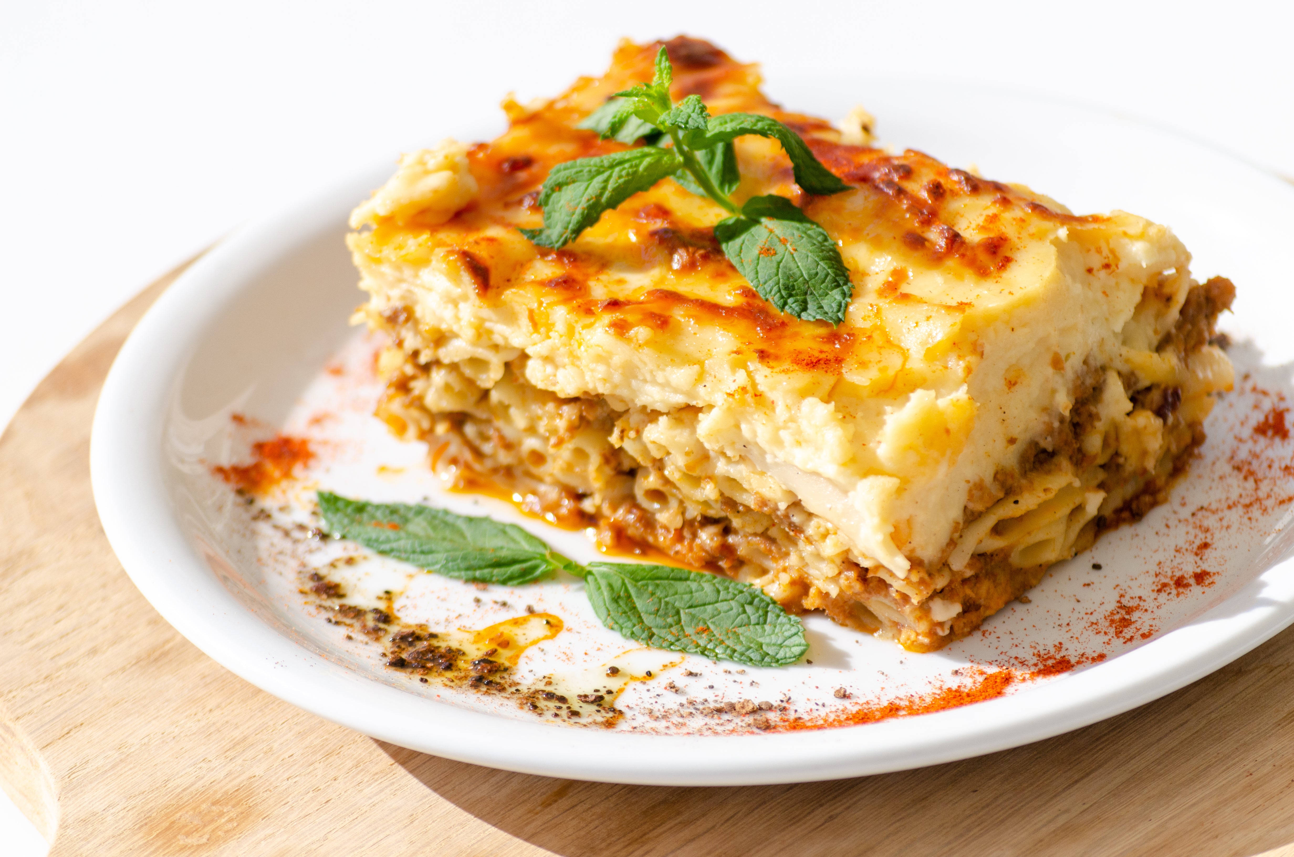 Food Photography 桌布 壁紙 — 金棕色分層希臘千層麵，配上融化起司和新鮮薄荷裝飾，放在白色盤子上。