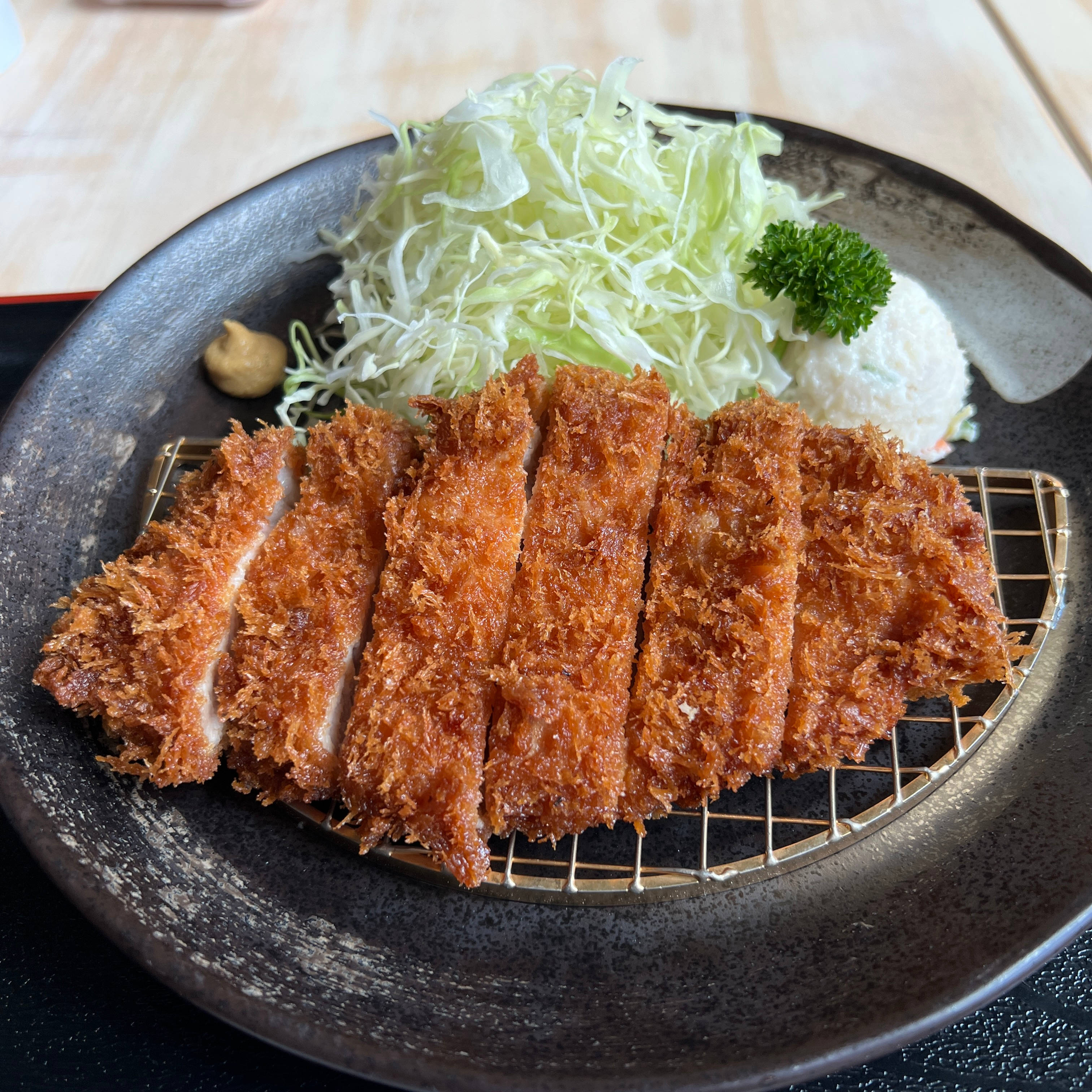 Food Photography 桌布 壁紙 — 金棕色切片炸豬排放在金屬架上，配以高麗菜絲、米飯和歐芹，置於深色陶瓷盤上。