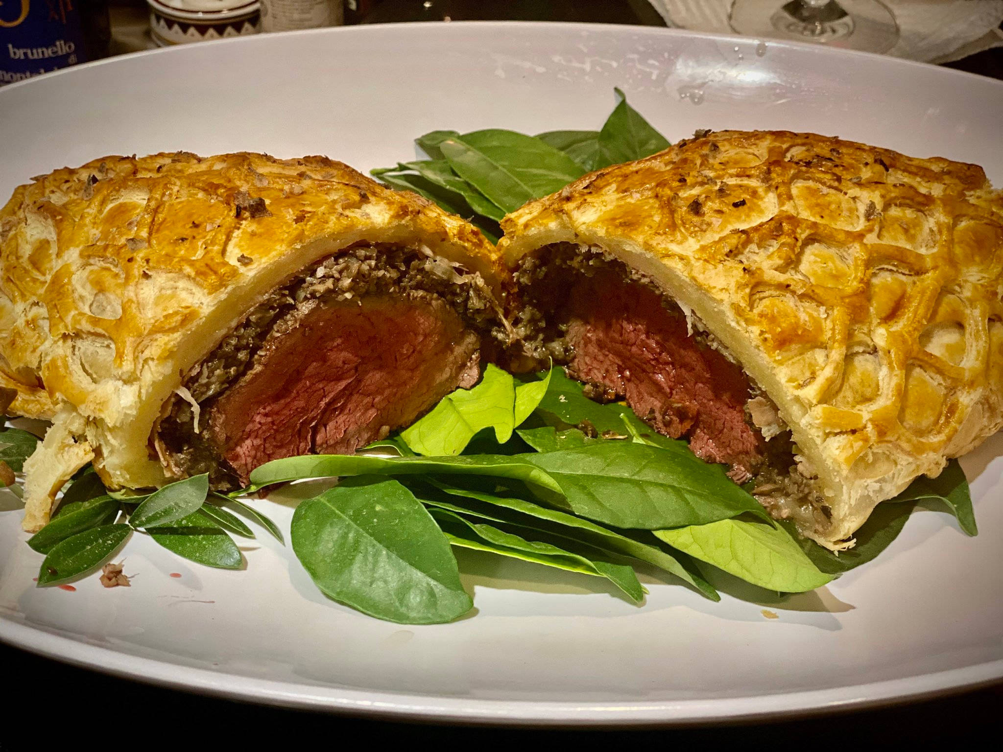 leafy 桌布 壁紙 — 金棕色威靈頓牛排切半，露出多汁的 medium-rare 牛肉和蒔蘿香草脆皮，放在新鮮菠菜葉上。