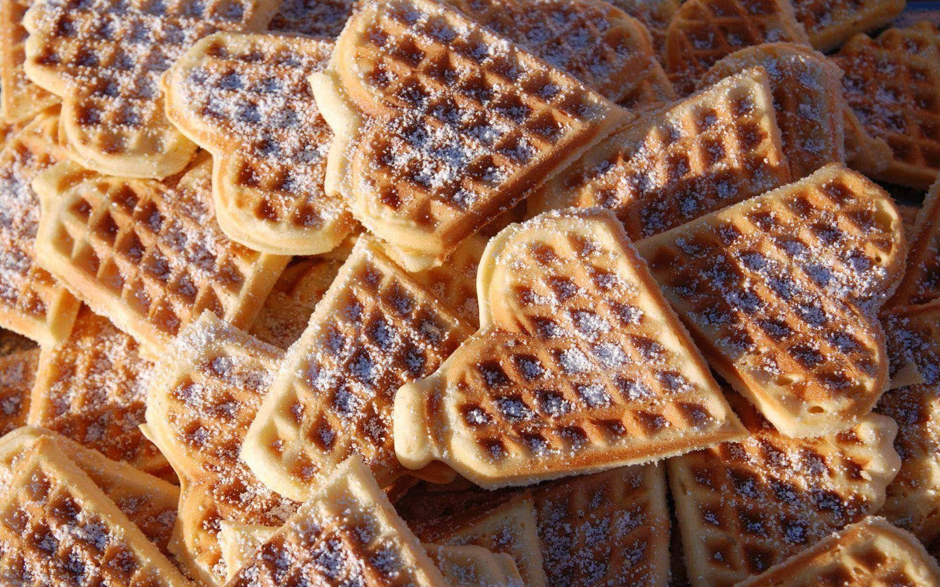 Waffle 桌布 壁紙 — 金棕色心形鬆餅的特寫，撒上糖粉，誘人地堆疊在一起。