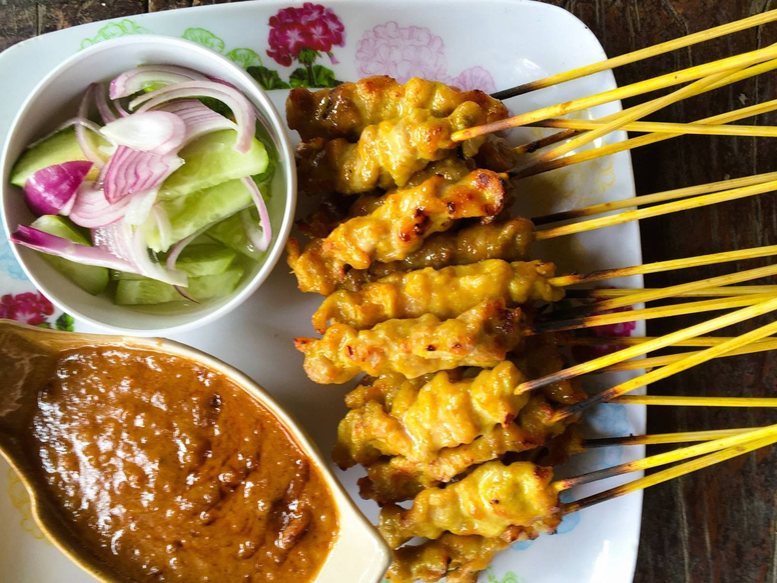 Delicious Food 桌布 壁紙 — 金棕色烤沙嗲串塗上醬汁，旁邊放著一碗切片小黃瓜和洋蔥，以及一池濃郁的花生醬，放在花卉圖案的盤子上。