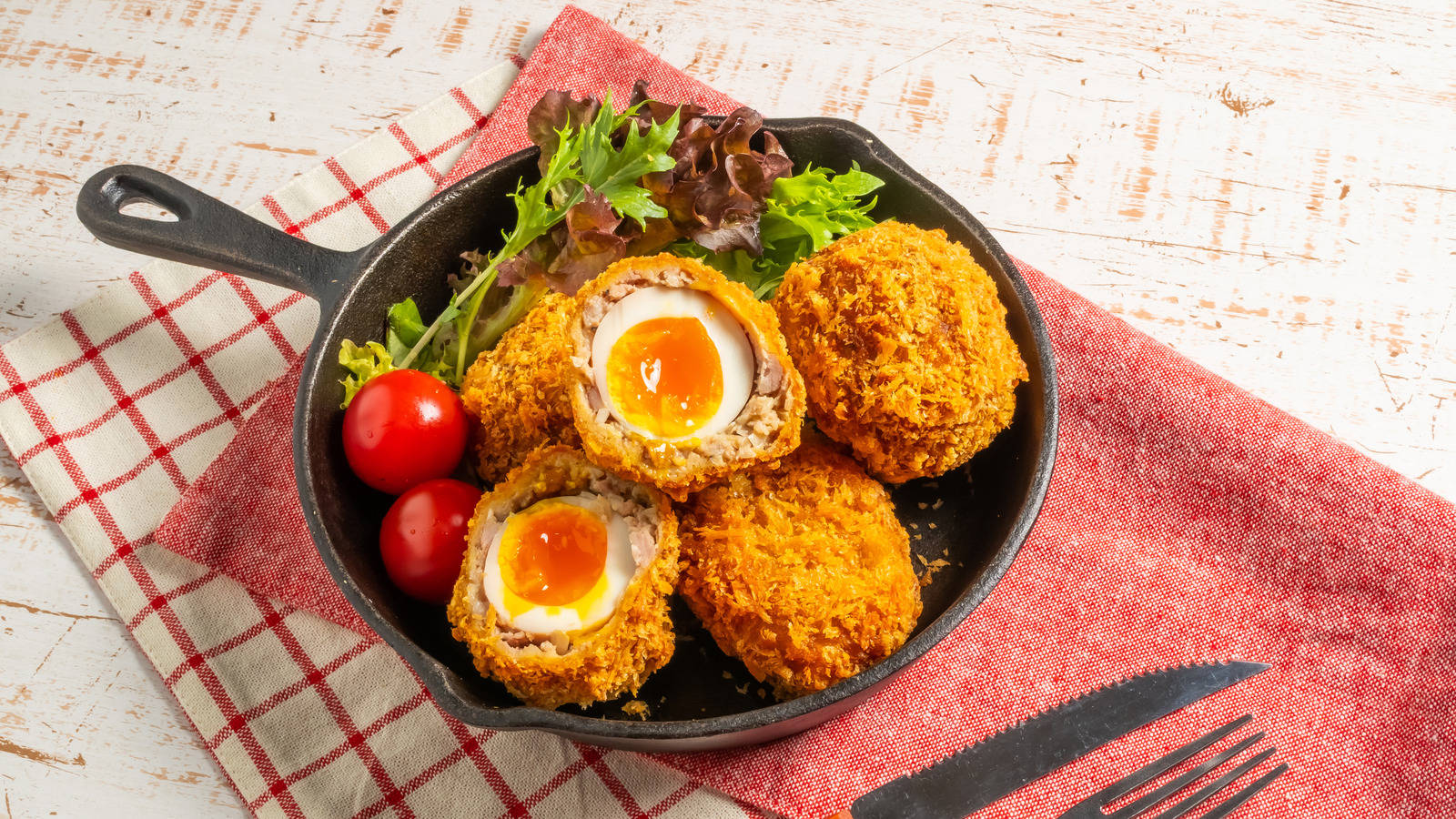 Egg 桌布 壁紙 — 金棕色蘇格蘭蛋，流心蛋黃置於鑄鐵煎鍋中，放在紅色格子餐巾上。