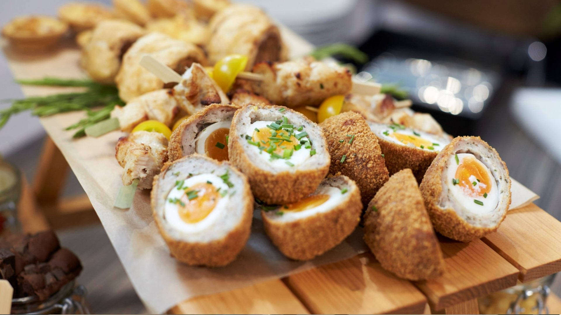 Egg 桌布 壁紙 — 金棕色蘇格蘭蛋切片，露出流心蛋黃，並以新鮮細香蔥裝飾在木製上菜板上。