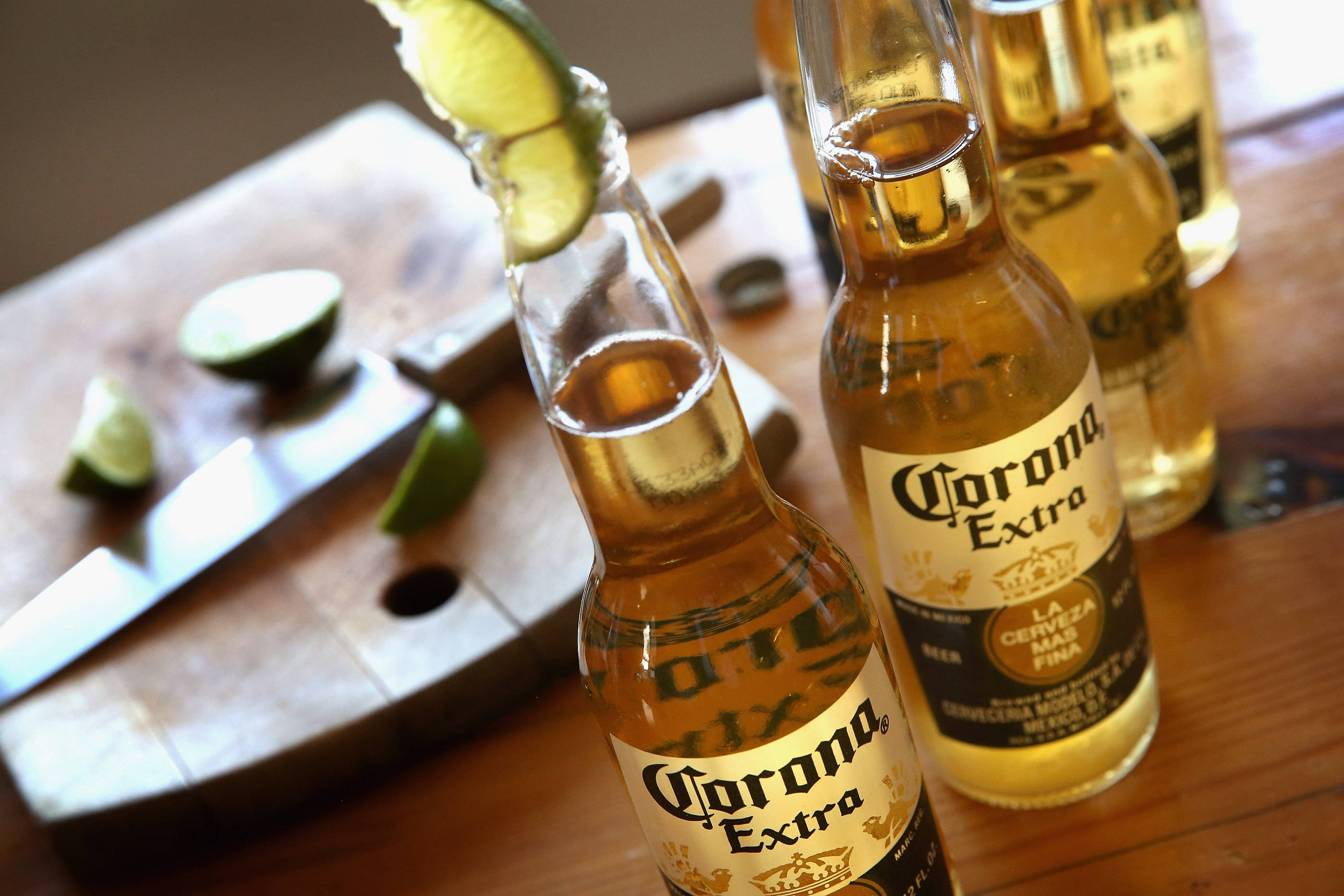 Lime 桌布 壁紙 — 金色 Corona Extra 啤酒瓶搭配萊姆角放在木桌上，旁邊有砧板放著萊姆片和一把刀。