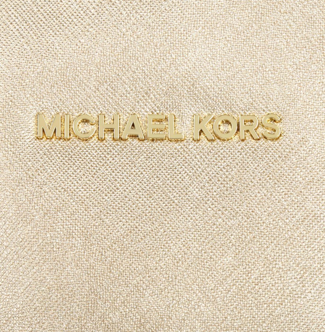 麥可·寇斯 桌布 壁紙 — 金色 Michael Kors 標誌近距離特寫，位於帶有精細編織細節的紋理米色布料上。
