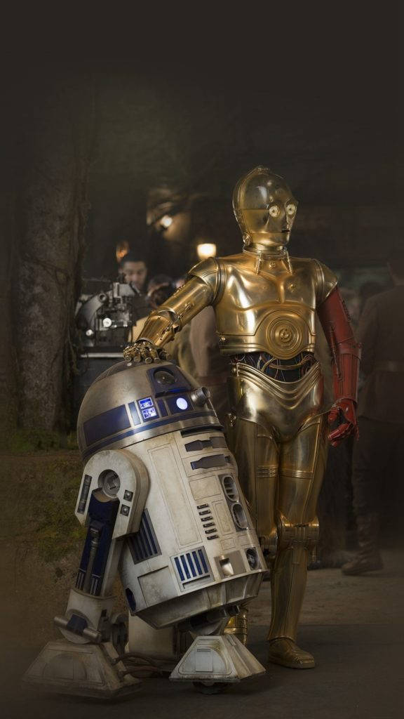 藝術 iPhone 桌布 壁紙 — 金色C-3PO和凹陷的R2-D2在夜晚昏暗的森林中並肩站立，背景有工作人員。
