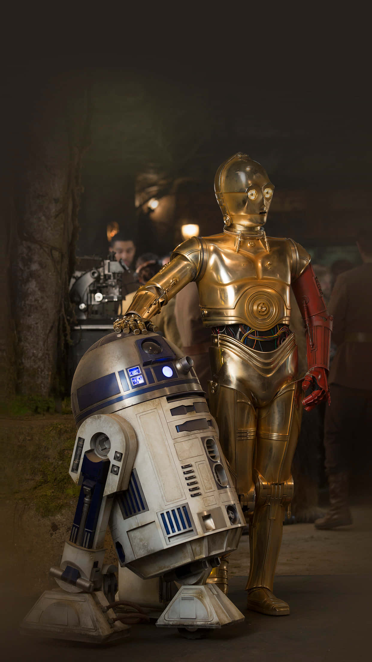r2d2 桌布 壁紙 — 金色C-3PO和藍白色R2-D2並排站在光線昏暗的森林場景中，背後有模糊的人影。