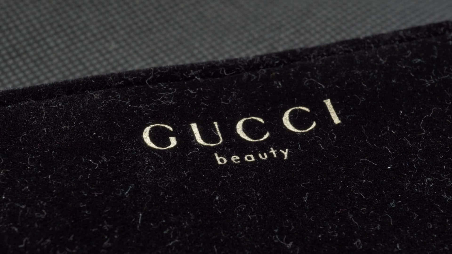 Gucci 桌布 壁紙 — 金色Gucci beauty標誌近距離特寫，繡在豪華黑色天鵝絨上，背景為紋理灰色。