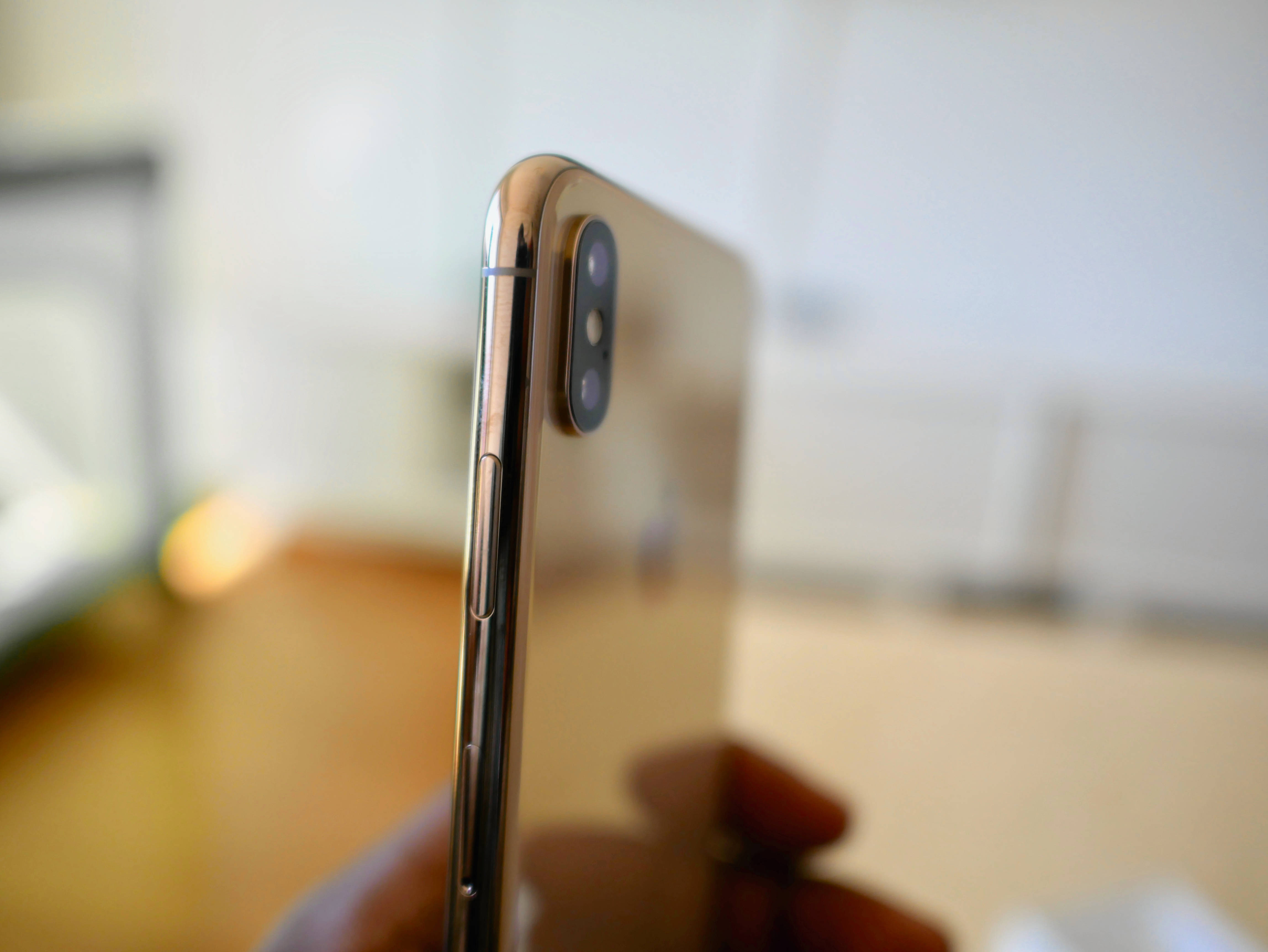 iPhone Xs Max 桌布 壁紙 — 金色iPhone X手持特寫，模糊的室內背景。
