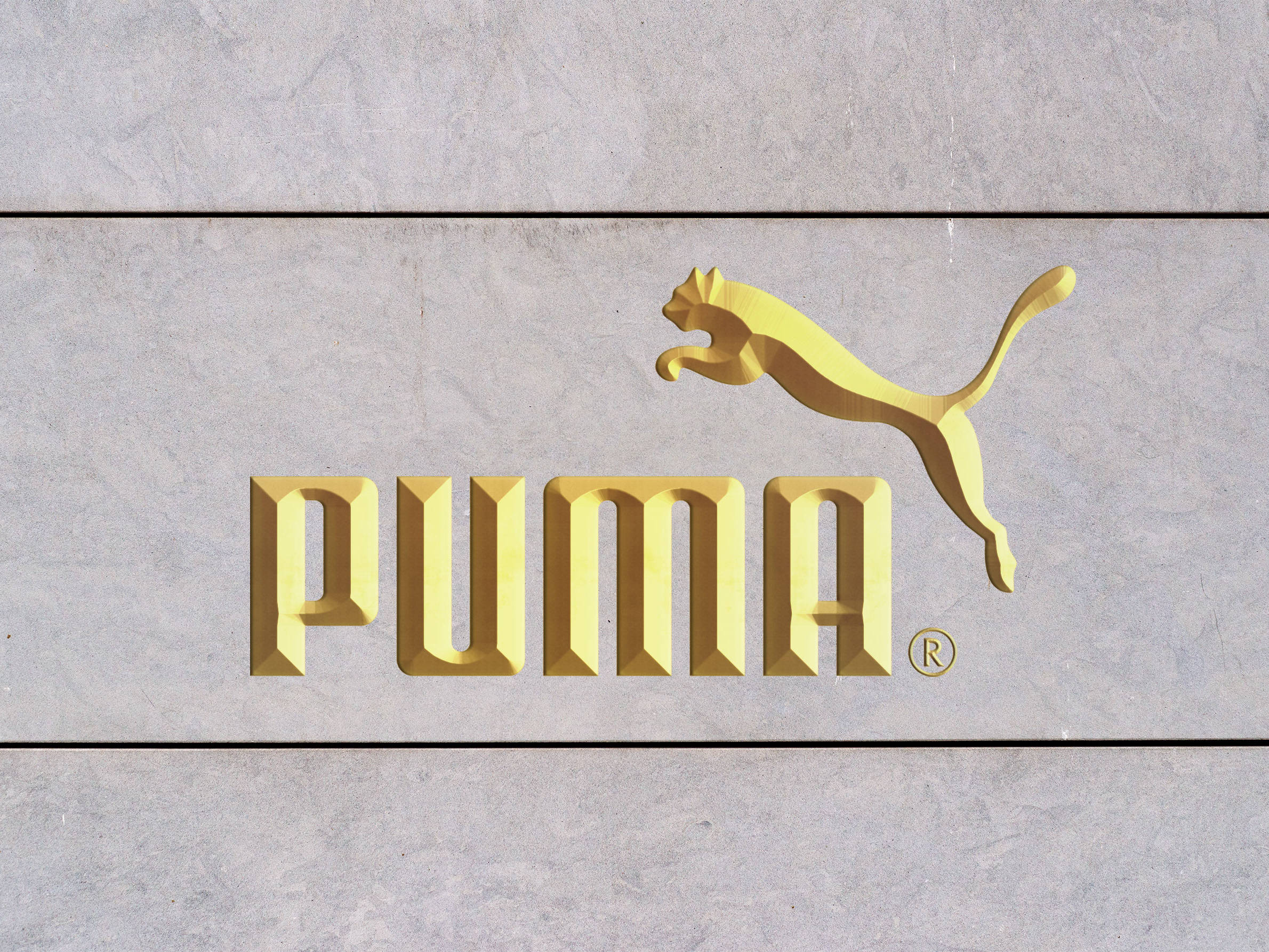 Puma 桌布 壁紙 — 金色Puma標誌，帶有跳躍貓標誌，安裝在紋理灰色石牆上。