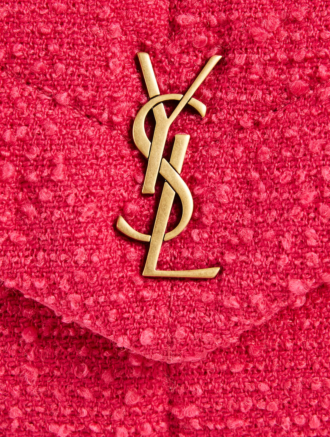 YSL 桌布 壁紙 — 金色YSL字母組合標誌的特寫，位於質感熱粉紅色粗花呢布料上。