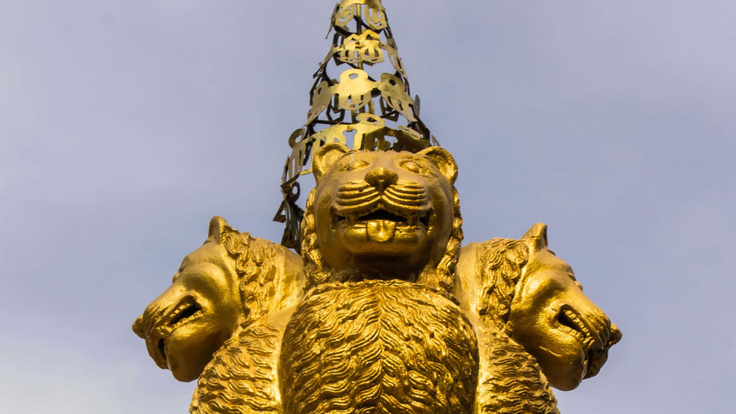statue 桌布 壁紙 — 金色三頭獅子雕像，飾有華麗王冠，襯以淡藍天空。