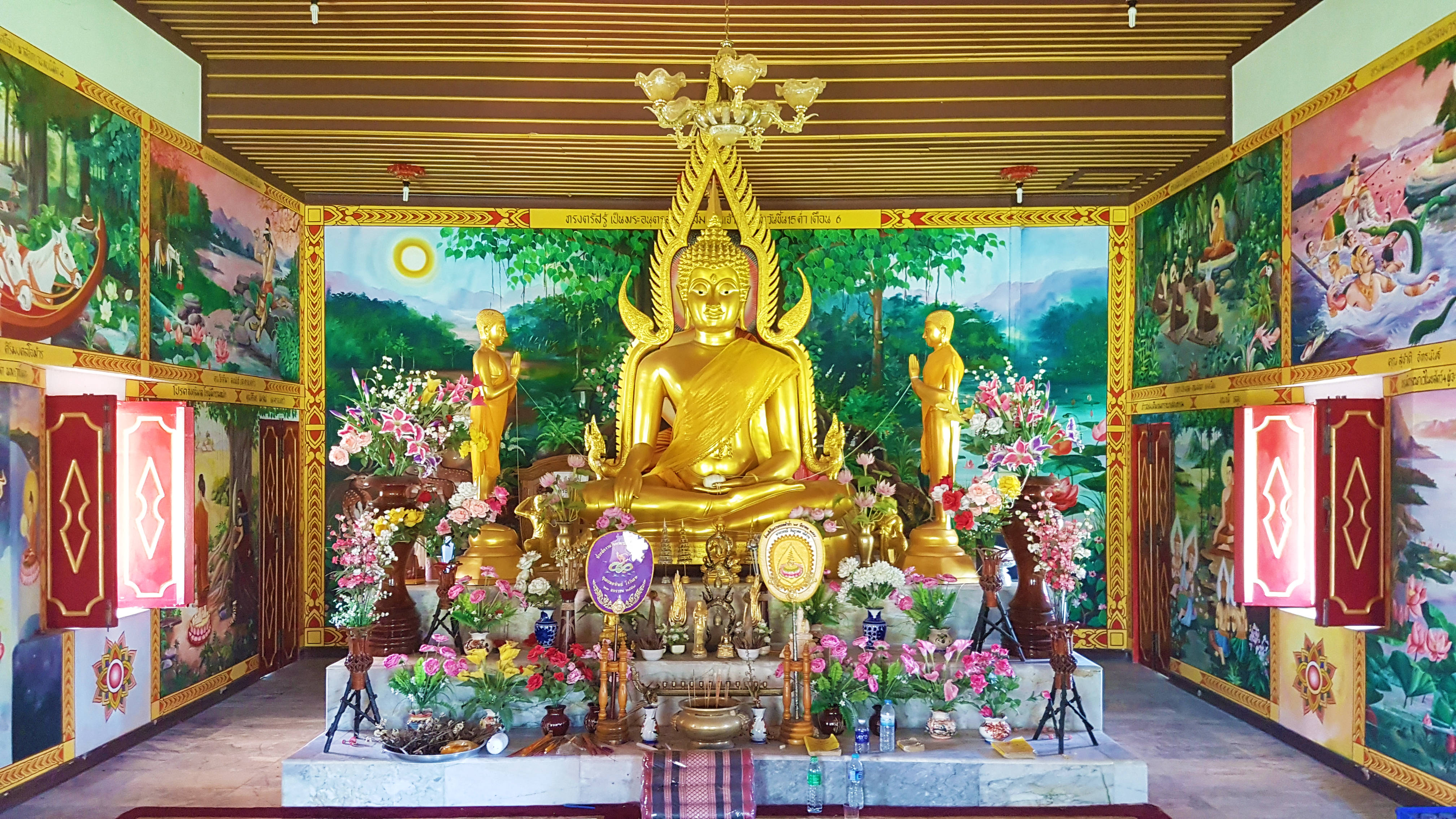 Gautam Buddha 桌布 壁紙 — 金色佛像靜靜地坐在一個裝飾著鮮豔花朵和供品的祭壇上，位於色彩繽紛的寺廟內部。